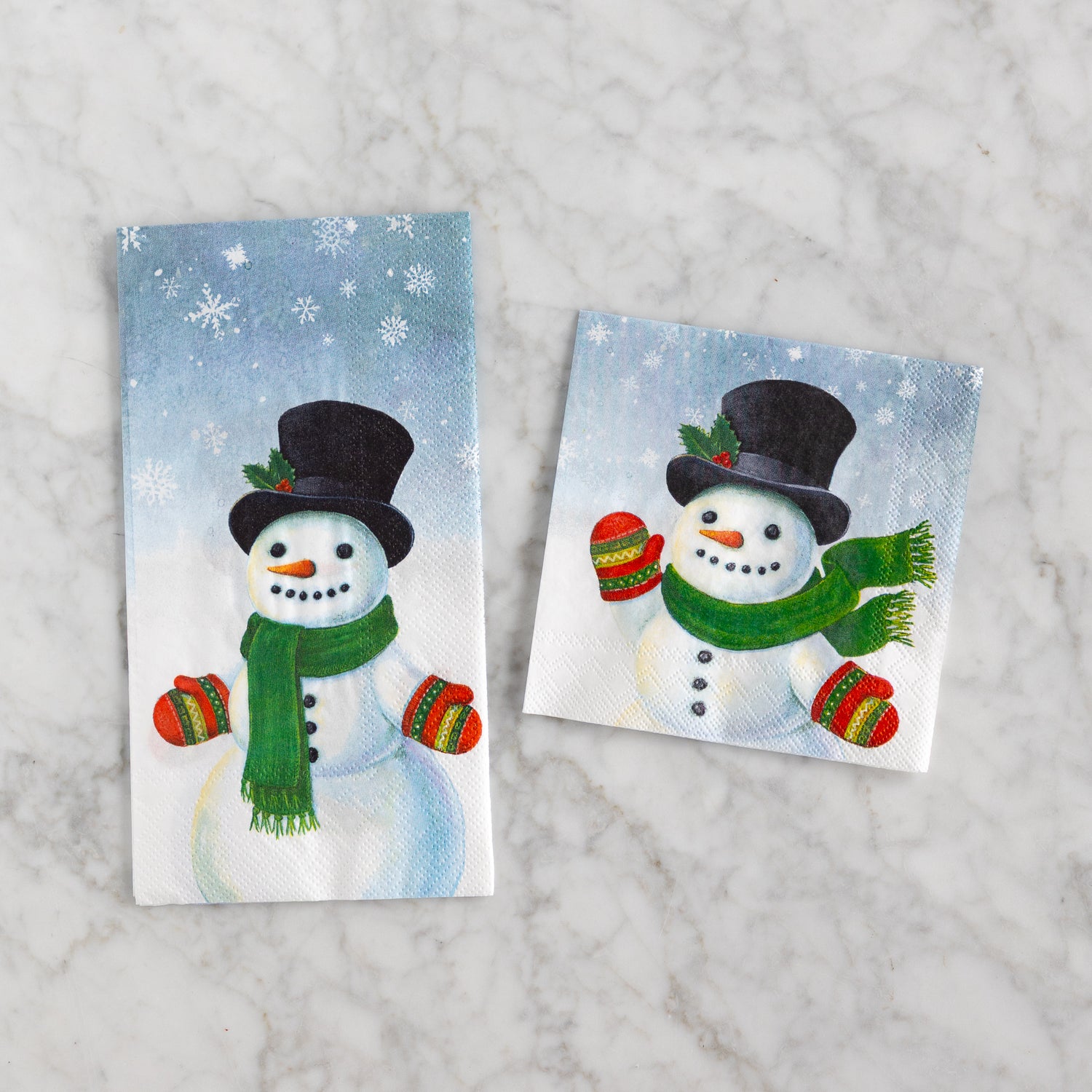 Two snowman-themed napkins with a winter background on a marble surface.