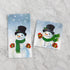 Two snowman-themed napkins with a winter background on a marble surface.