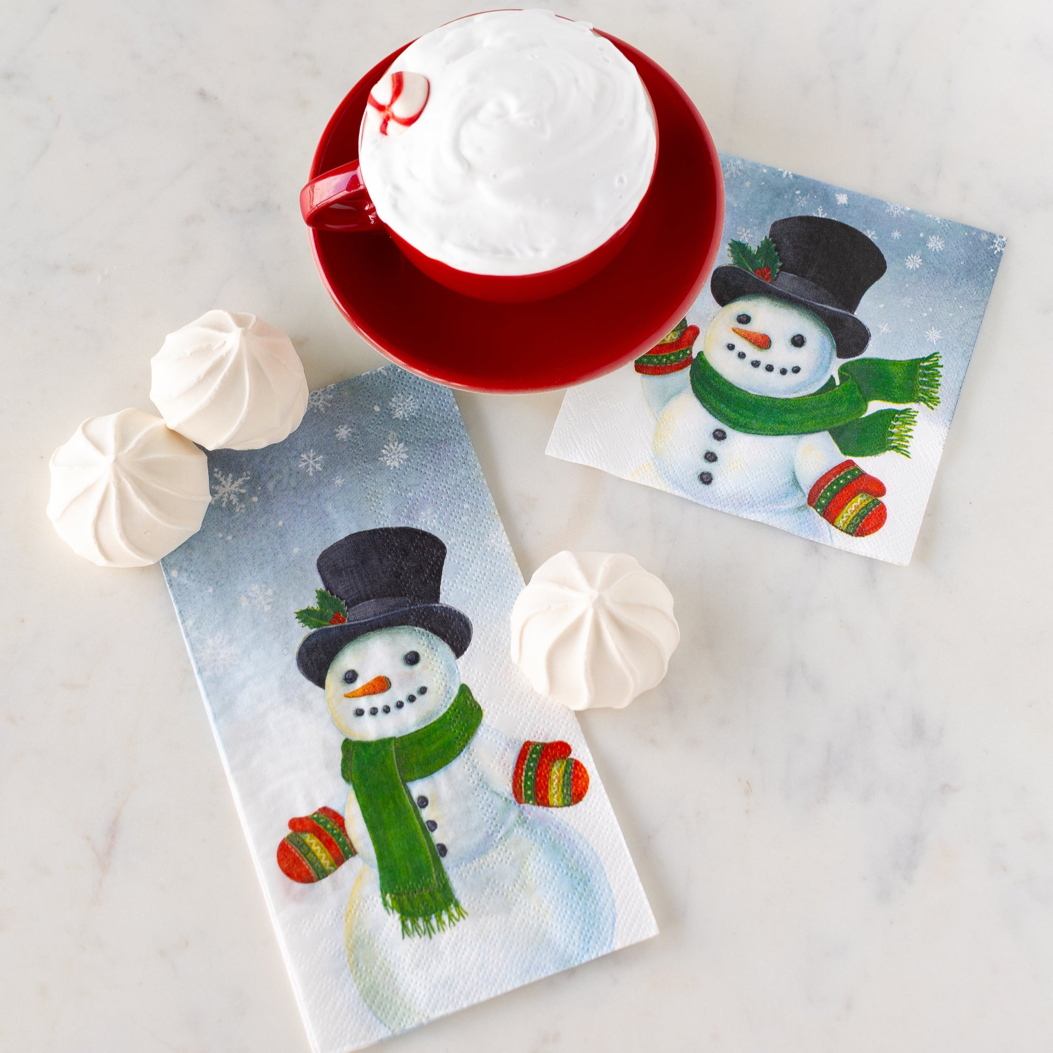 Snowman Cocktail and Guest Napkins on a table next to three treats and a cup filled with whip cream and a peppermint.