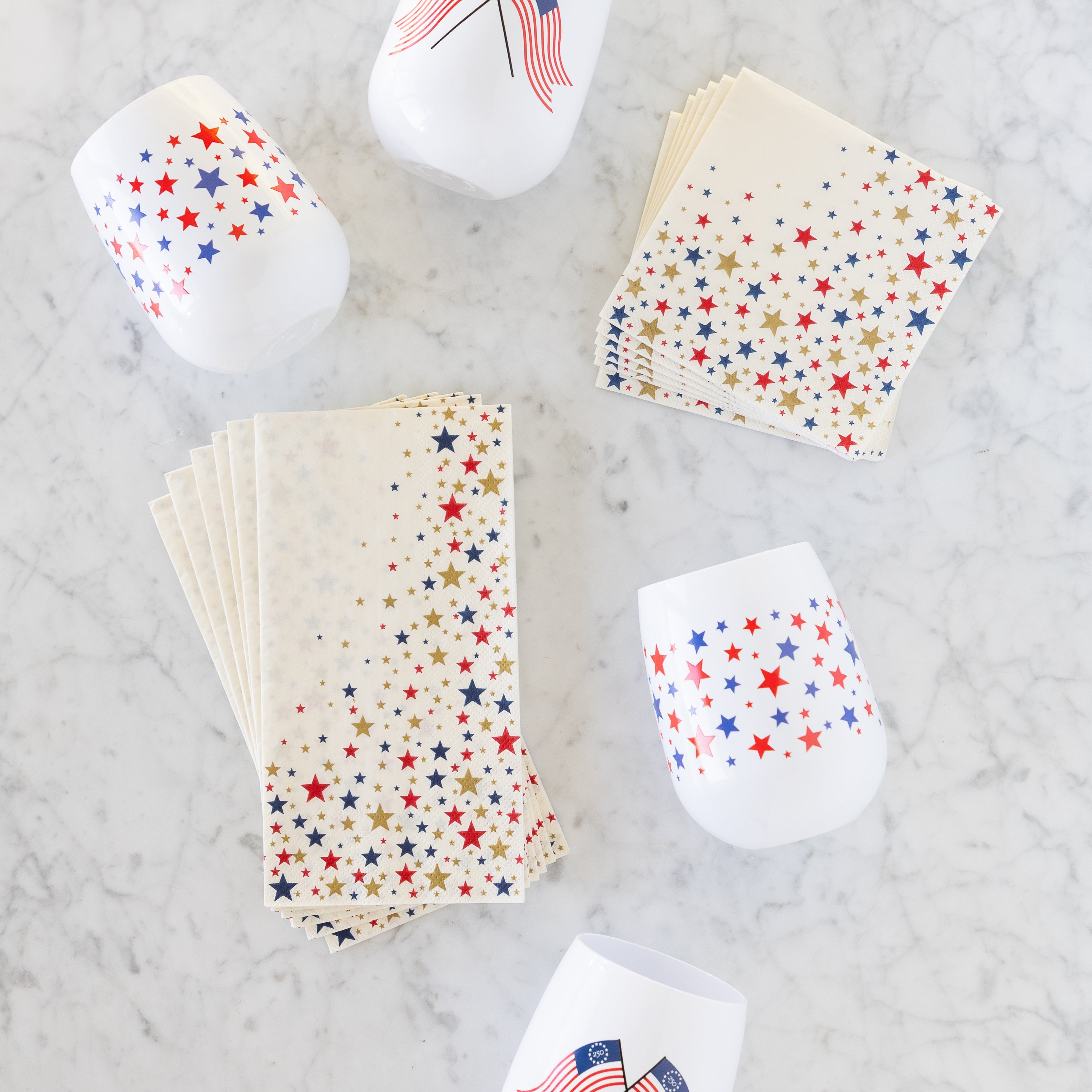A stack of Star-Spangled Guest and Cocktail Napkins on a marble table next to patriotic cups.