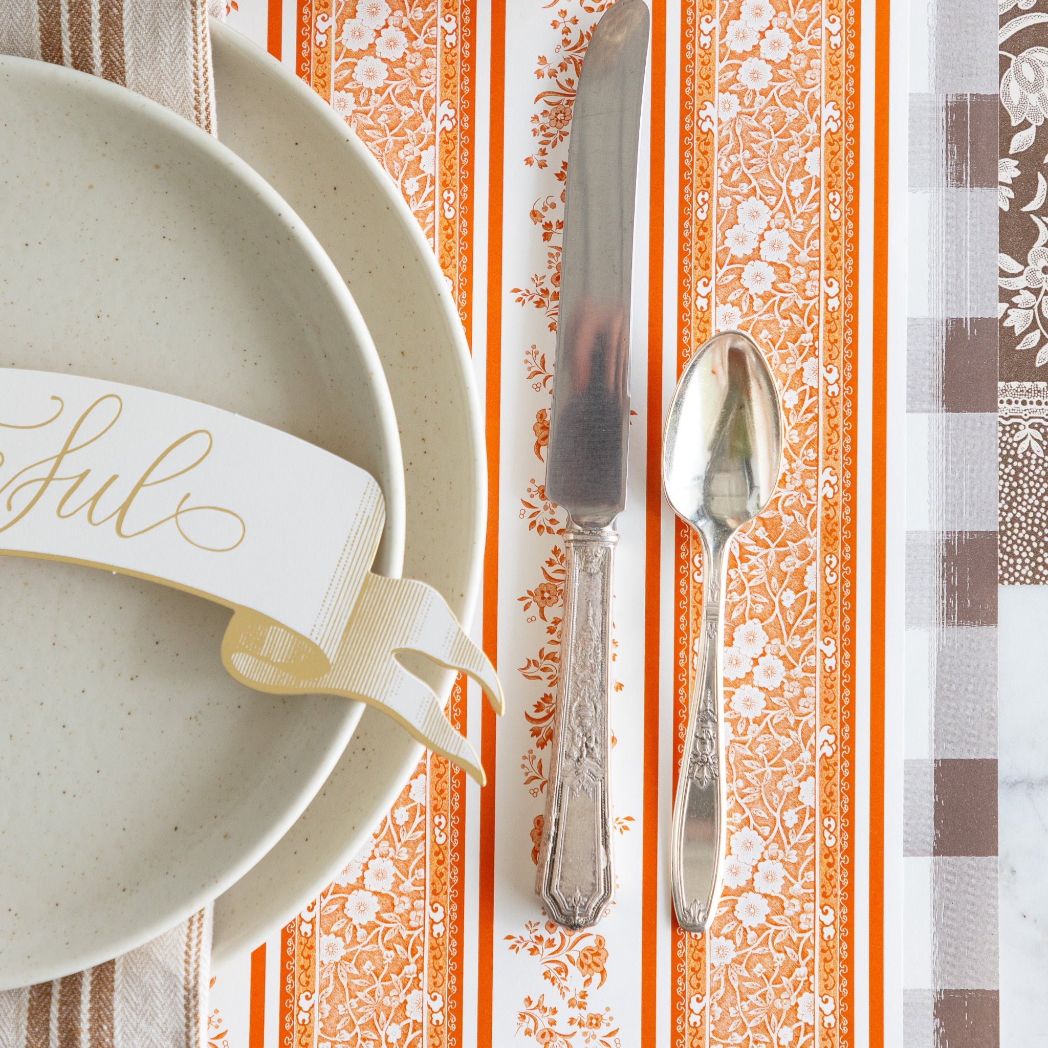 The Pumpkin Burleigh Stripe Placemat with vintage silverware, vanilla dinnerware, and Grateful Banner Table Accent atop, on the Brown Painted Check Runner.