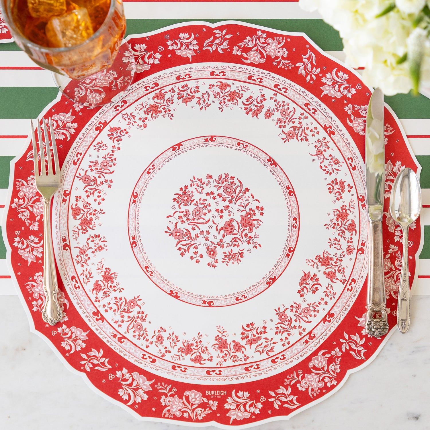 A place setting featuring the Die-cut Red Regal Placemat with vintage flatware and iced tea atop, and Green &amp; Red Awning Stripe Runner underneath.