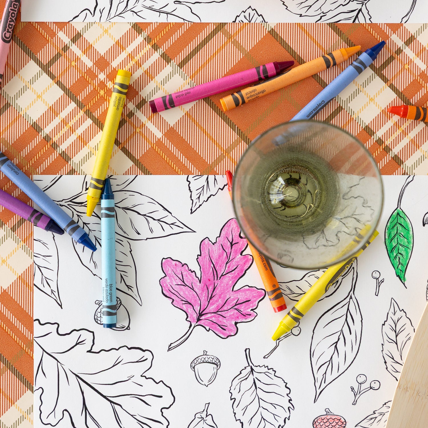 The Coloring Leaves Placemat partially colored in with an empty glass and scattered crayons on top and Orange Plaid Runner underneath.