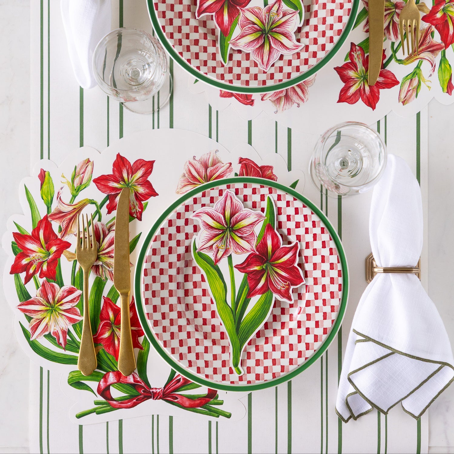 A place setting featuring the Die-cut Amaryllis Placemat with a green-rimmed and red-and white checkered plate and Amaryllis Table Accent atop, and gold flatware on the Antique Green Striped Runner.