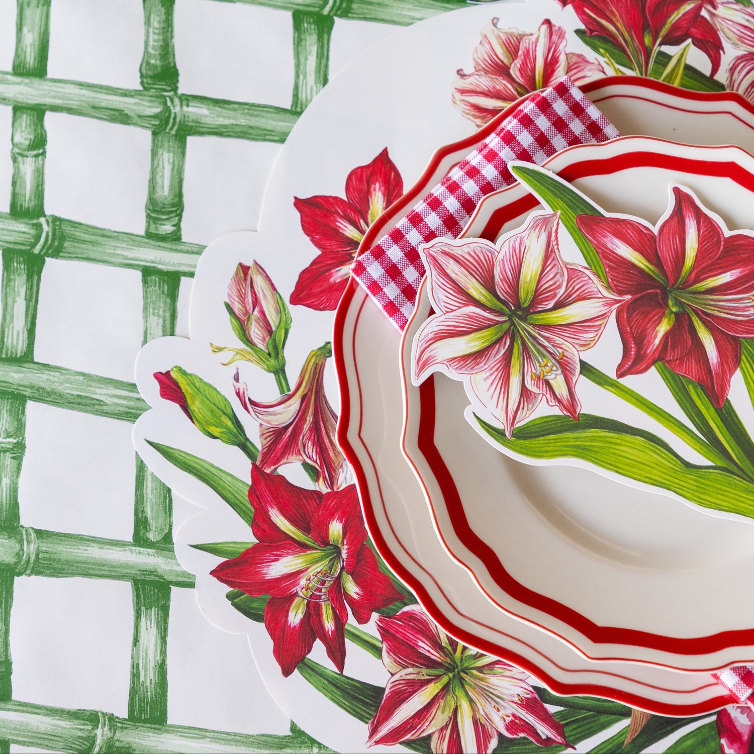 The Die-cut Amaryllis Placemat under red scalloped dinnerware, a red-and-white checkered napkin and Amaryllis Table Accent on the Green Lattice Runner.