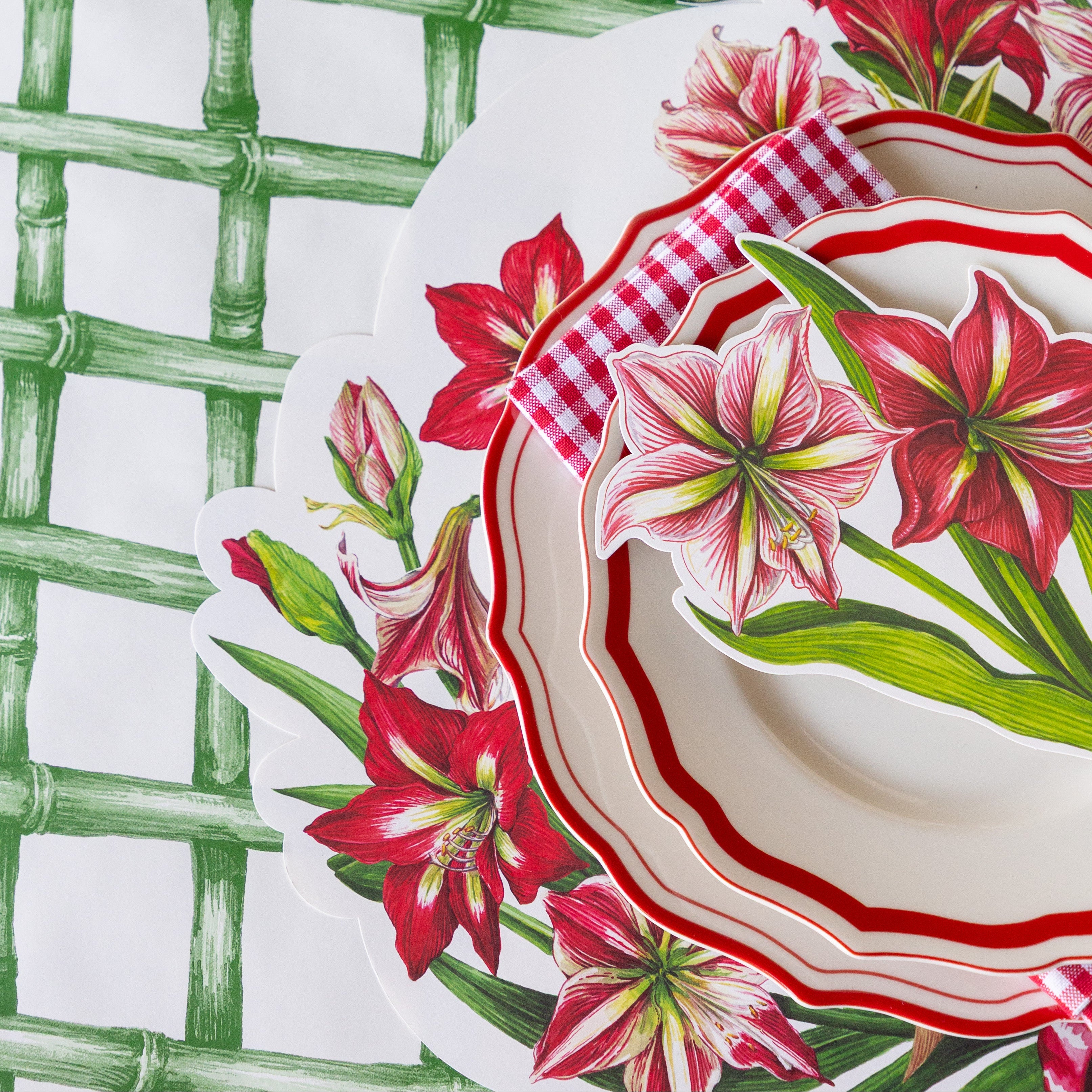 The Die-cut Amaryllis Placemat under red scalloped dinnerware, a red-and-white checkered napkin and Amaryllis Table Accent on the Green Lattice Runner.