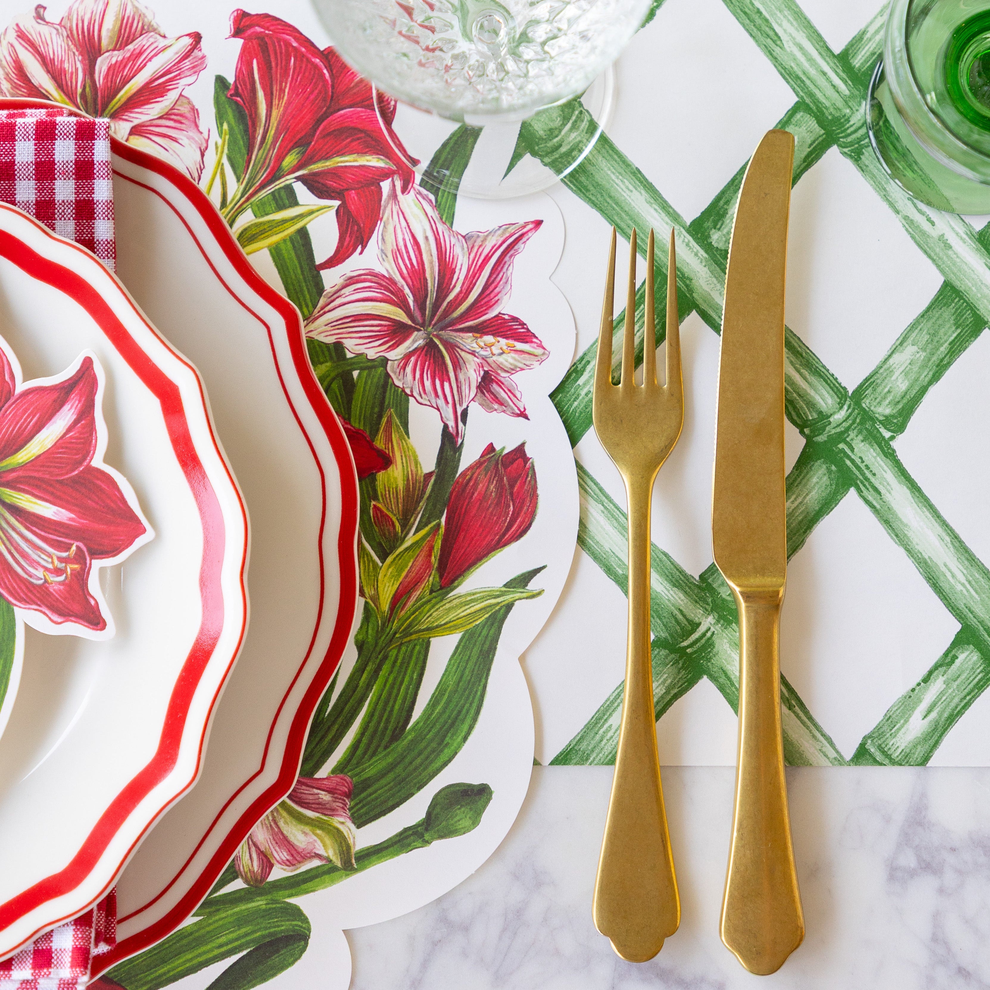 The Die-cut Amaryllis Placemat under dinnerware next to gold flatware on the Green Lattice Runner.