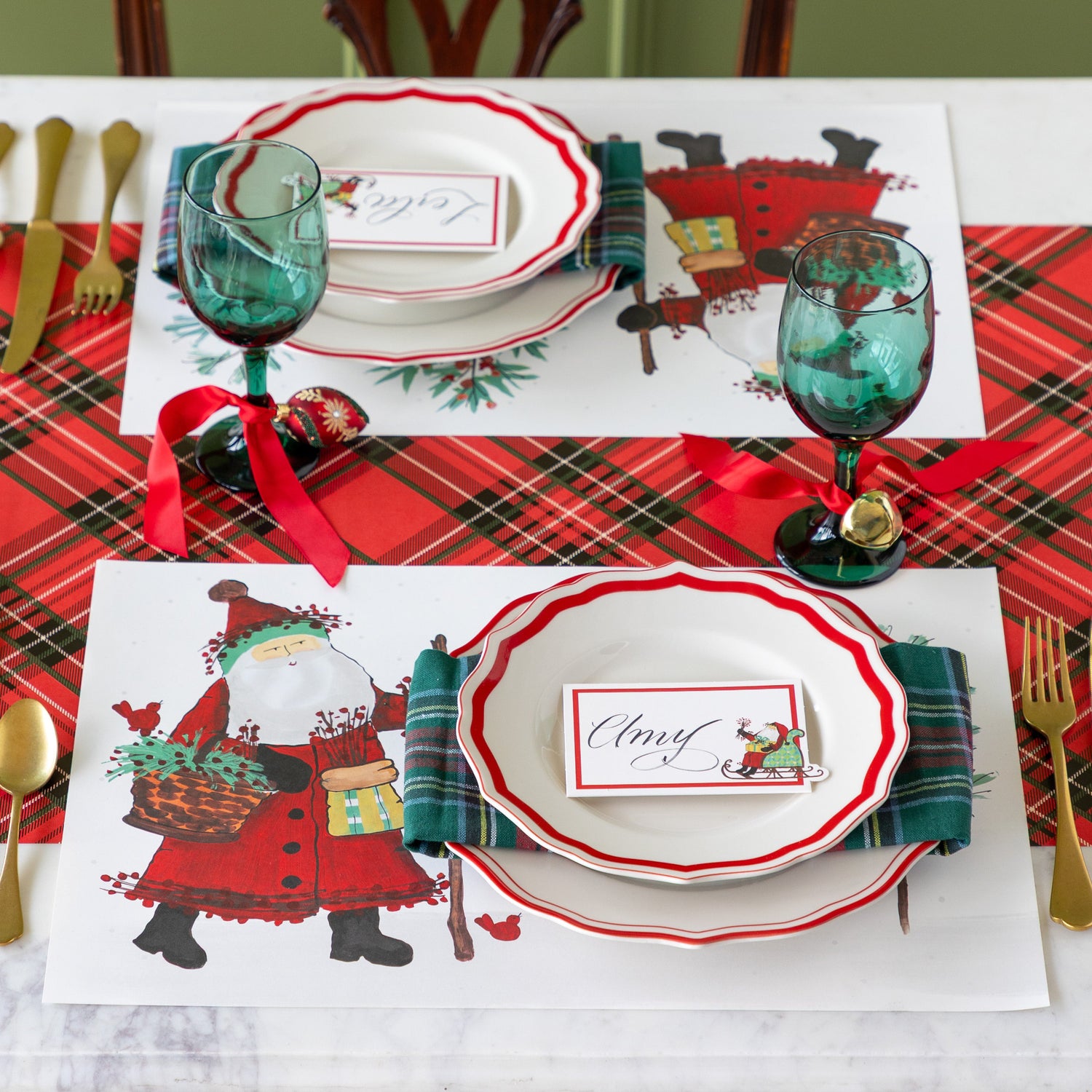 Christmas-themed table setting with Old St. Nick Forest Placemats, Red Icing on the Cake plates, Old St. Nick Sleigh Place Card, plaid napkins and gold flatware on the Red Plaid Runner. 