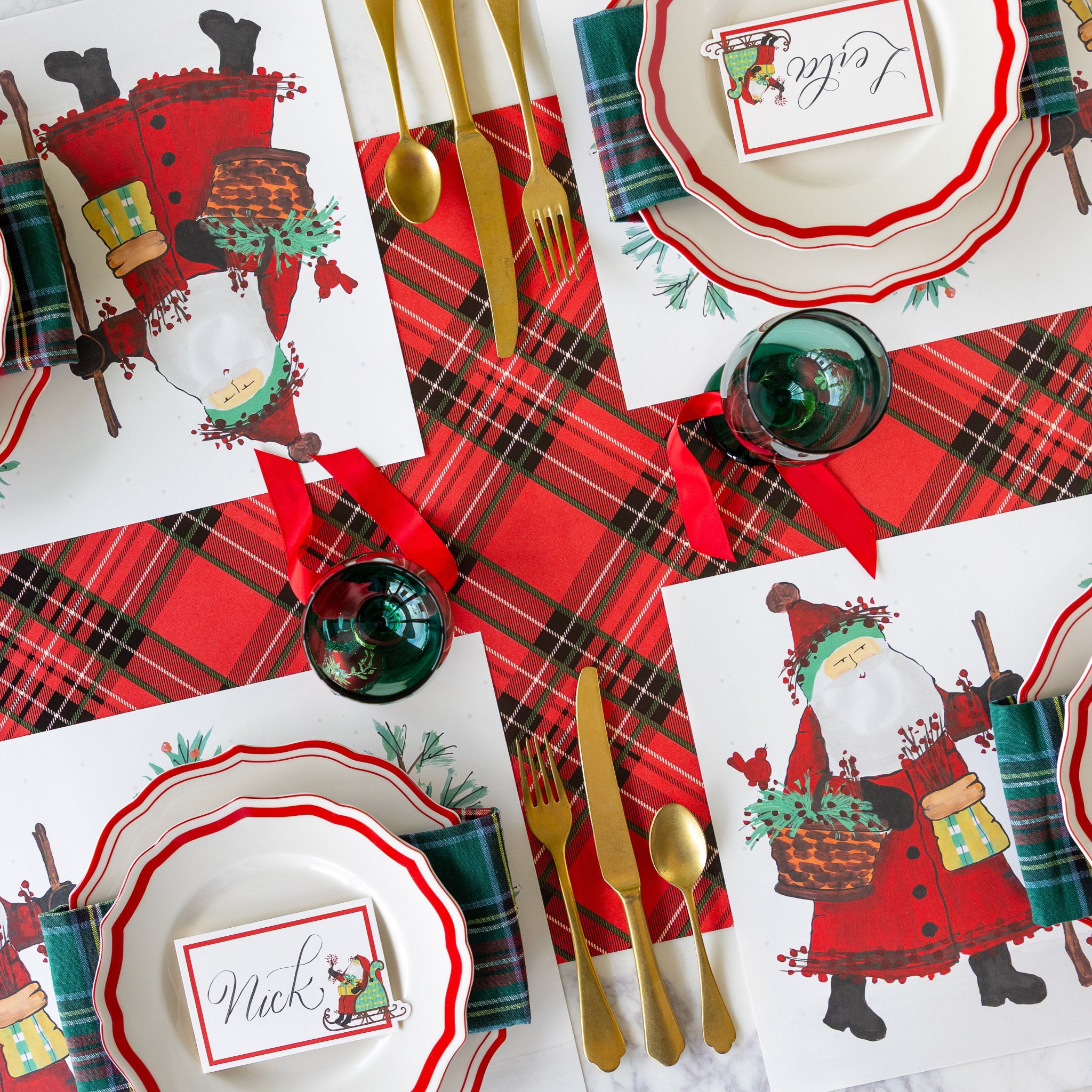 The Red Plaid Runner under a Christmas themed table setting featuring the Old St. Nick Forest Placemats, Red Icing on the Cake plates with Old St. Nick Sleigh Place Cards atop, and gold flatware.