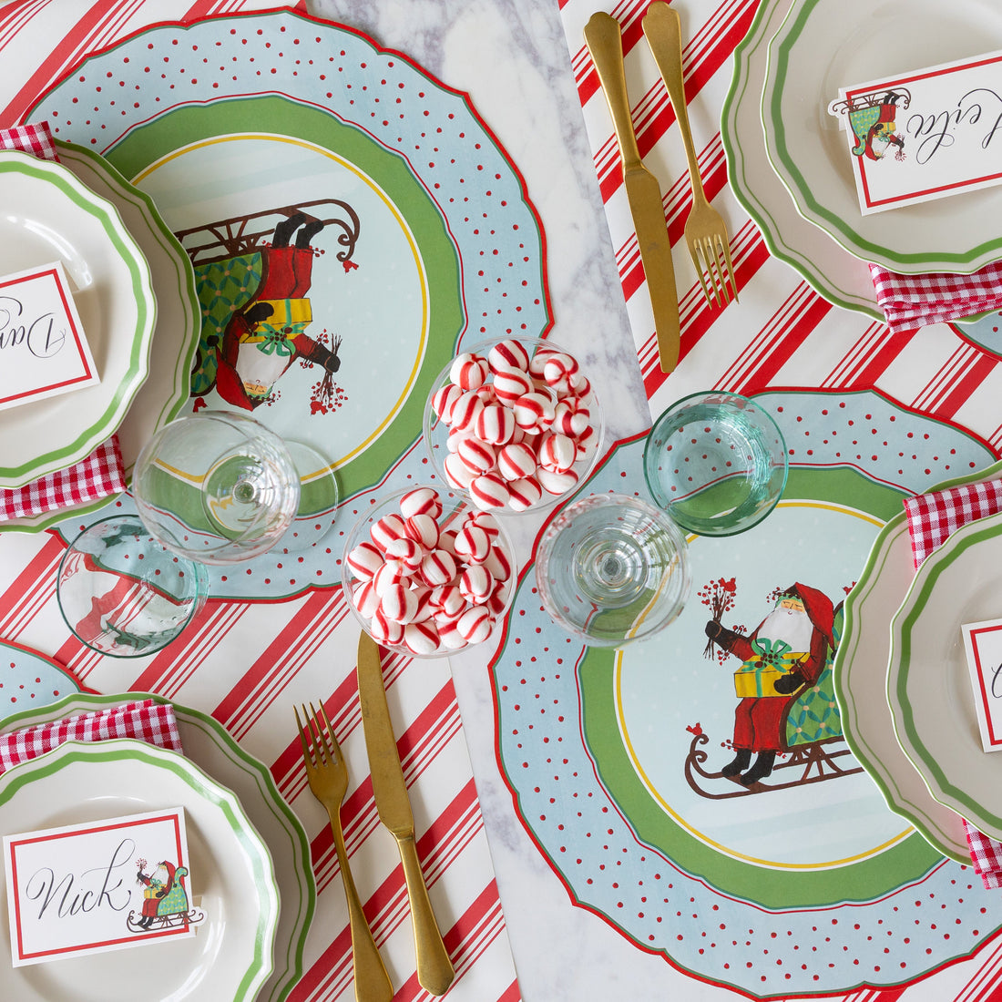 Christmas-themed table setting with Green Icing on the Cake plates, red-and-white checkered napkins, gold cutlery, cups of peppermints and Die-cut Old St. Nick Sleigh Placemat on the Peppermint Stripe Runner.