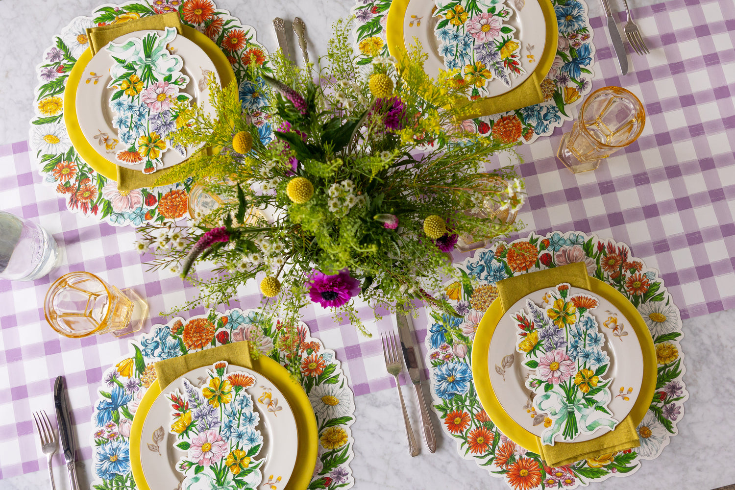 Table setting with a floral arrangement, Die-cut Wildflower Wreath Placemats, Wildflower Table Accents and colorful plates on the Lilac Painted Check Runner.