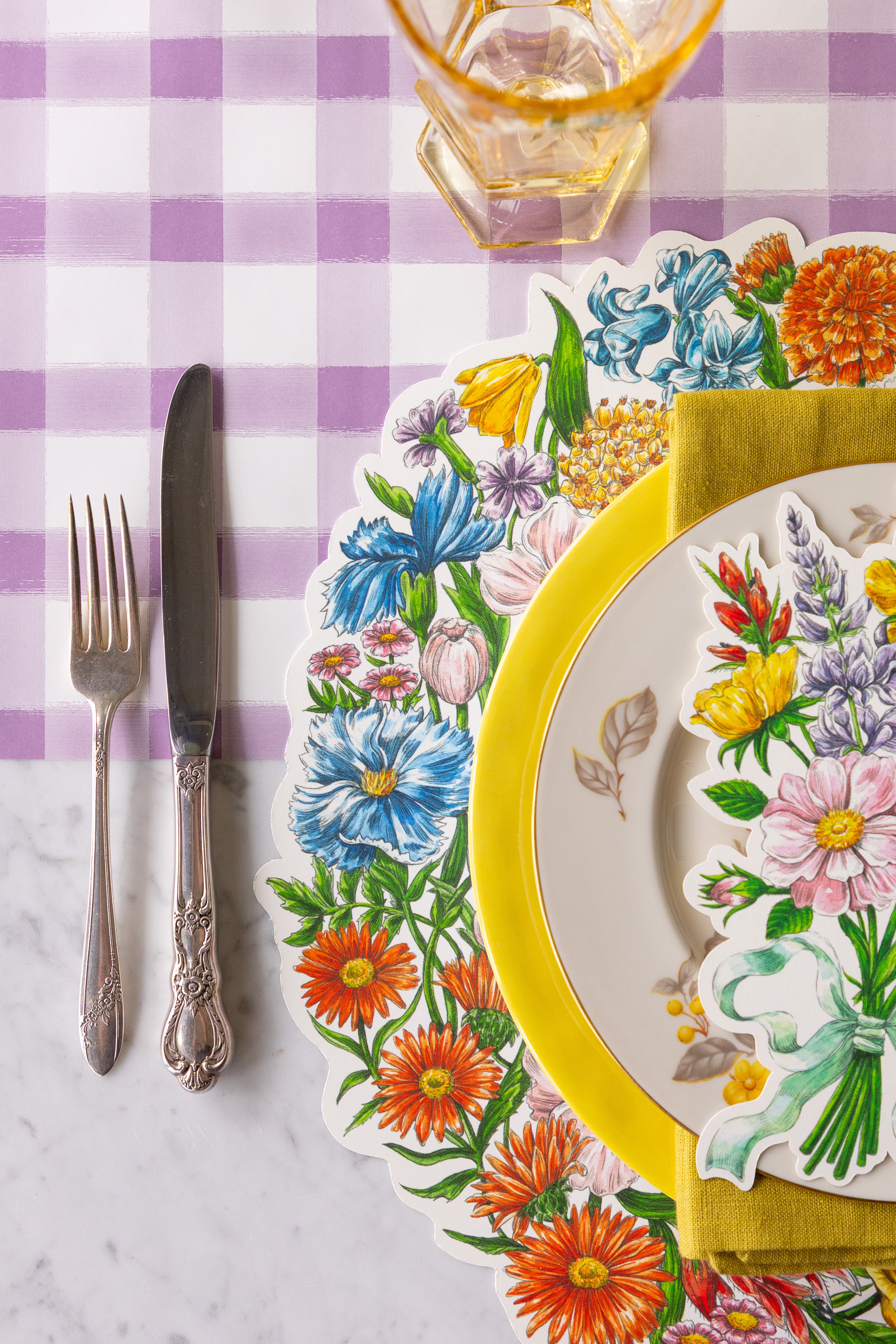 Table setting with Die-cut Wildflower Wreath Placemat, Wildflower Table Accent  and colorful plates on the Lilac Painted Check Runner.