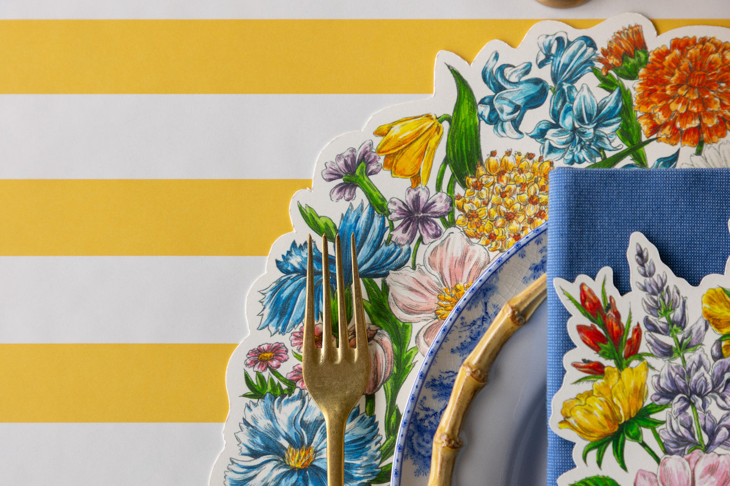 Table setting with Die-cut Wildflower Wreath Placemat, floral and bamboo plates, blue napkin, Wildflower Table Accent and gold cutlery on the Marigold Classic Stripe Runner.