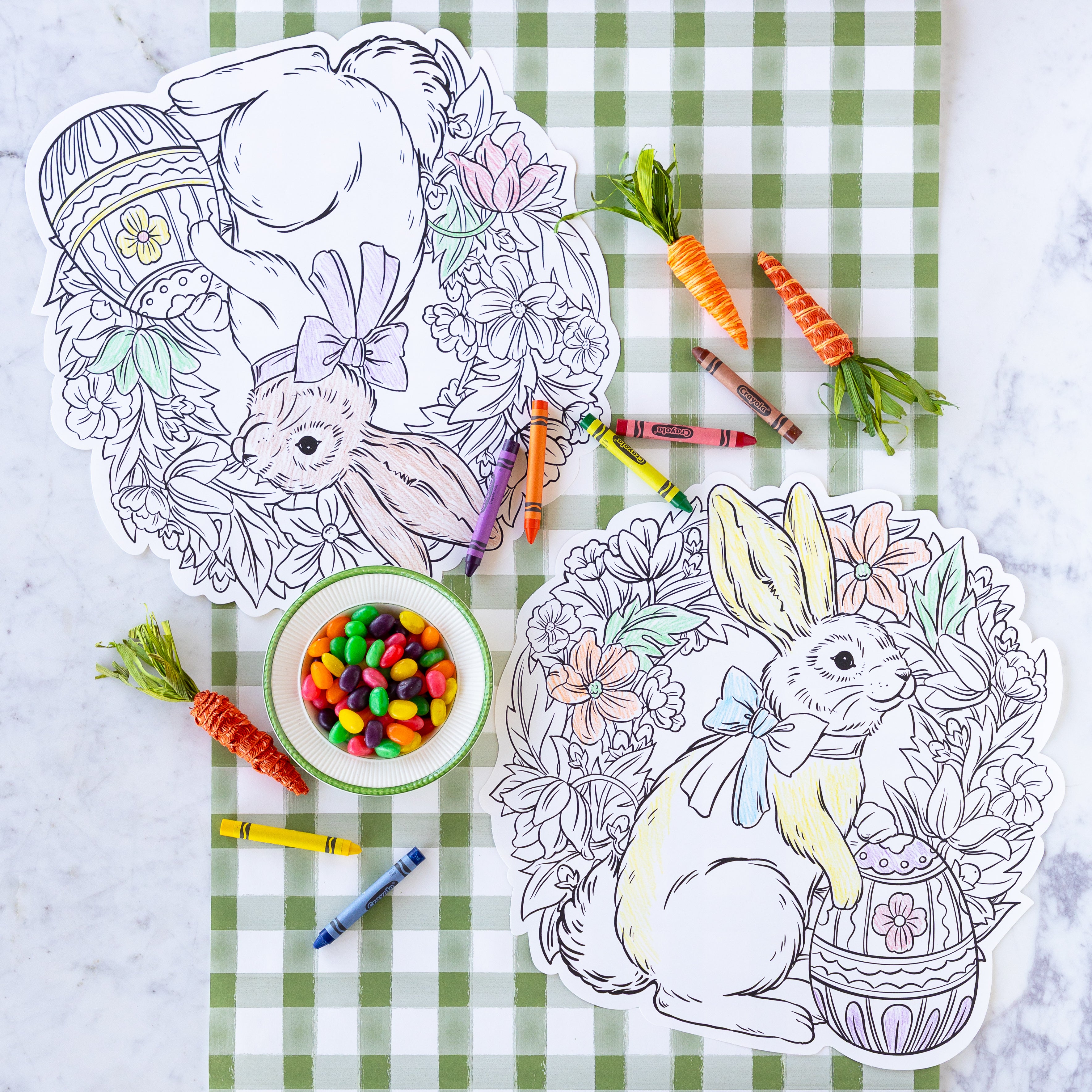 A table with Die-cut Coloring Bunny Wreath Placemats, bowl of jelly beans, crayons and carrots.