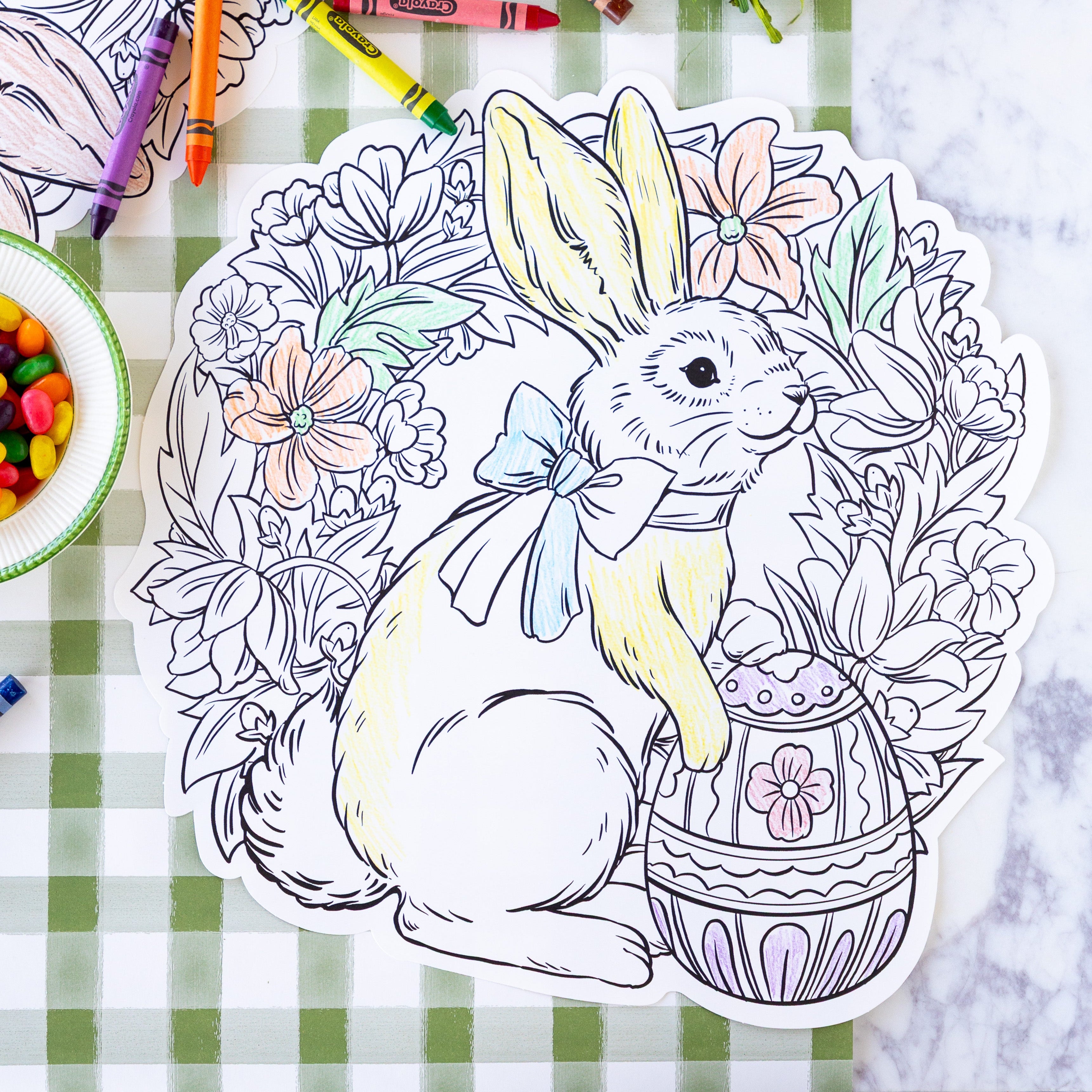 Die-cut Coloring Bunny Wreath Placemat partially colored in on a table with crayons and jelly beans.