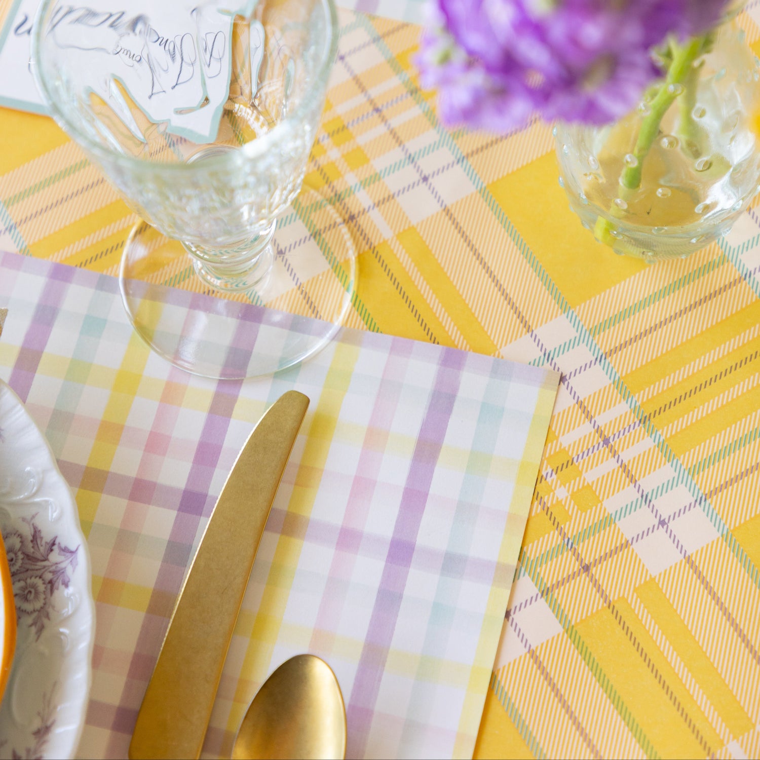 Dining table setting with Spring Plaid Placemat, glass, cutlery, and floral arrangement on the Yellow Plaid Runner.