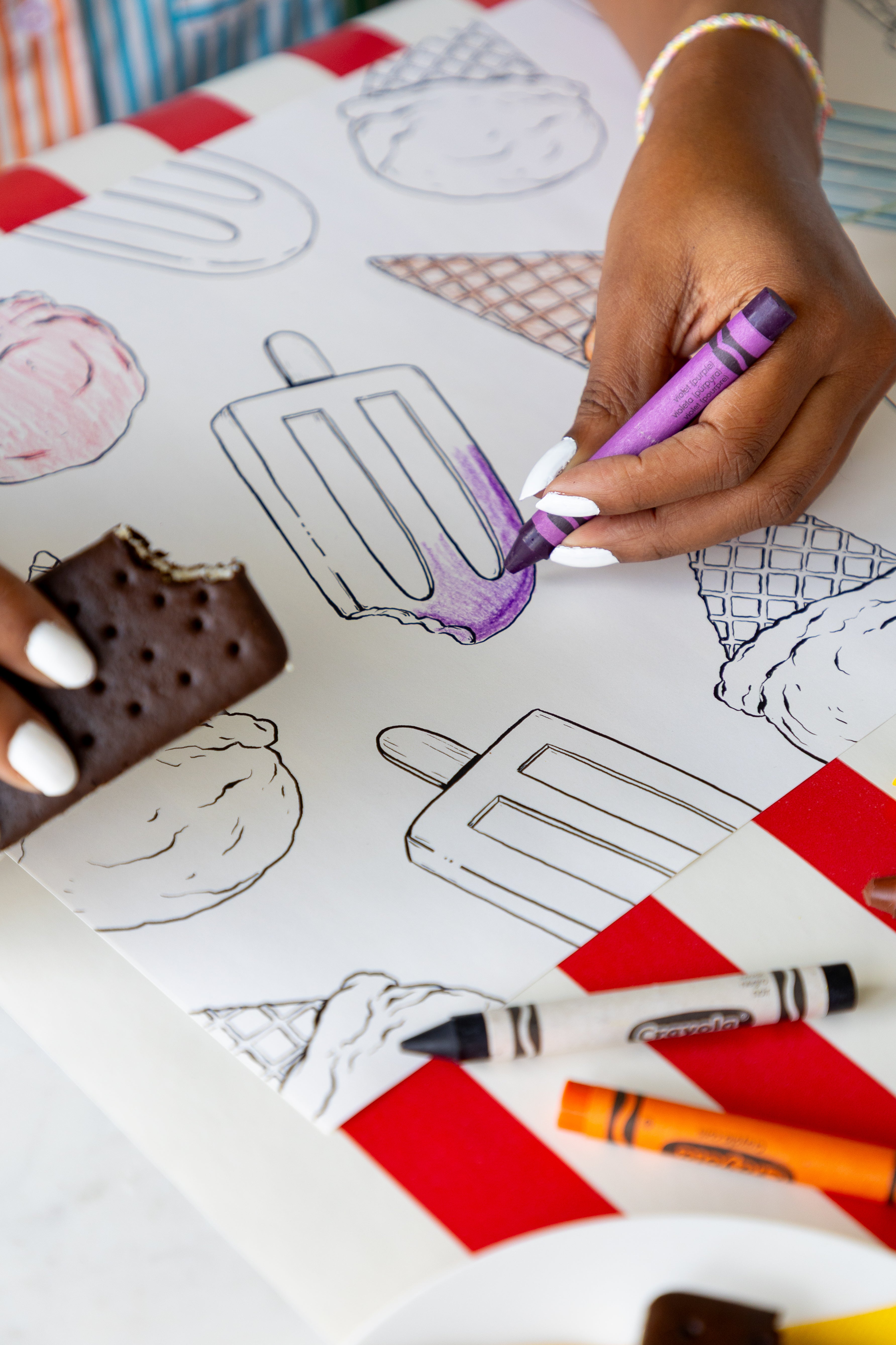 A person coloring the Coloring Summer Treats Placemats with crayons on a table with the Red Classic Stripe Runner.