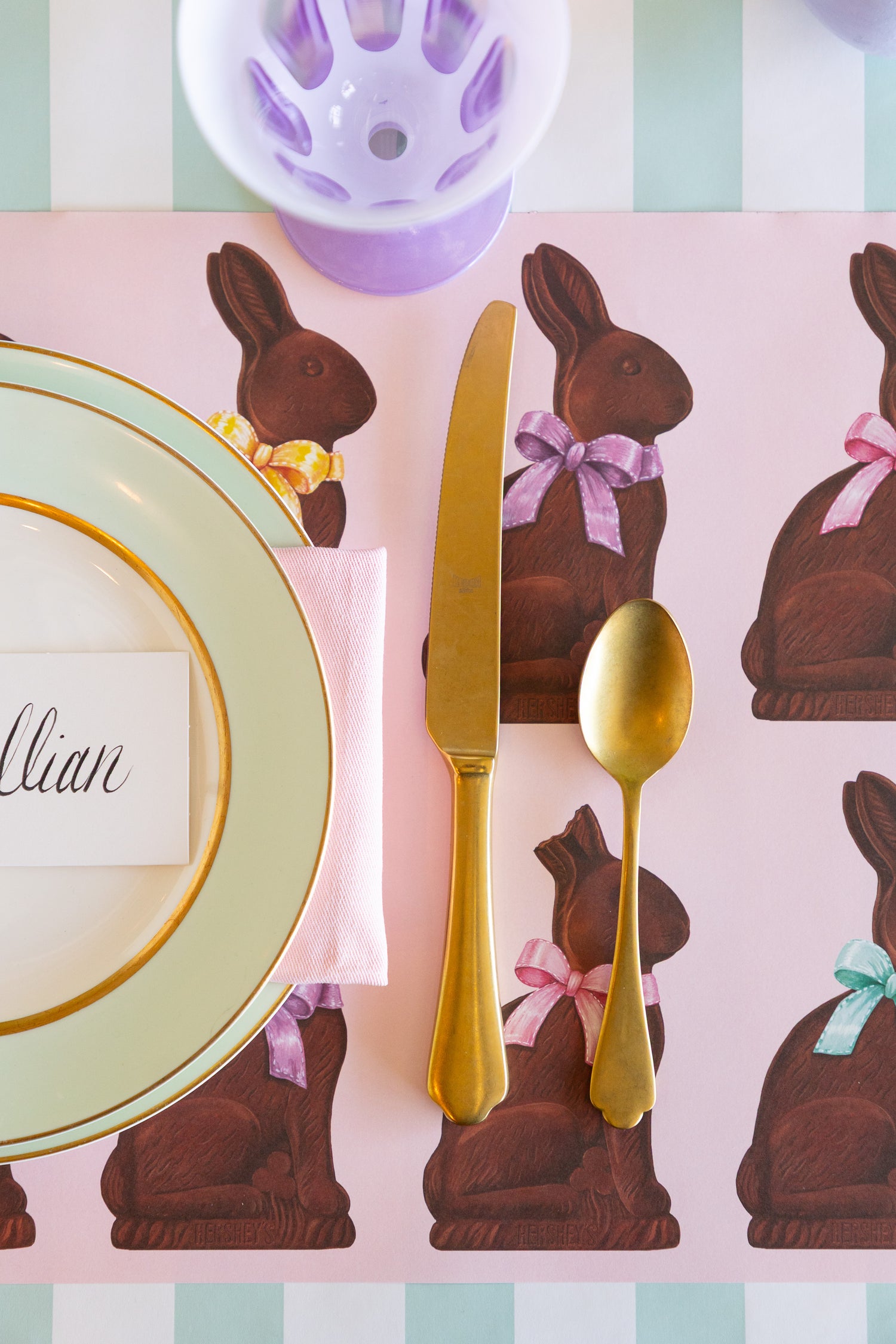 Easter-themed place setting with chocolate bunny placemats, gold cutlery, and pastel colors.