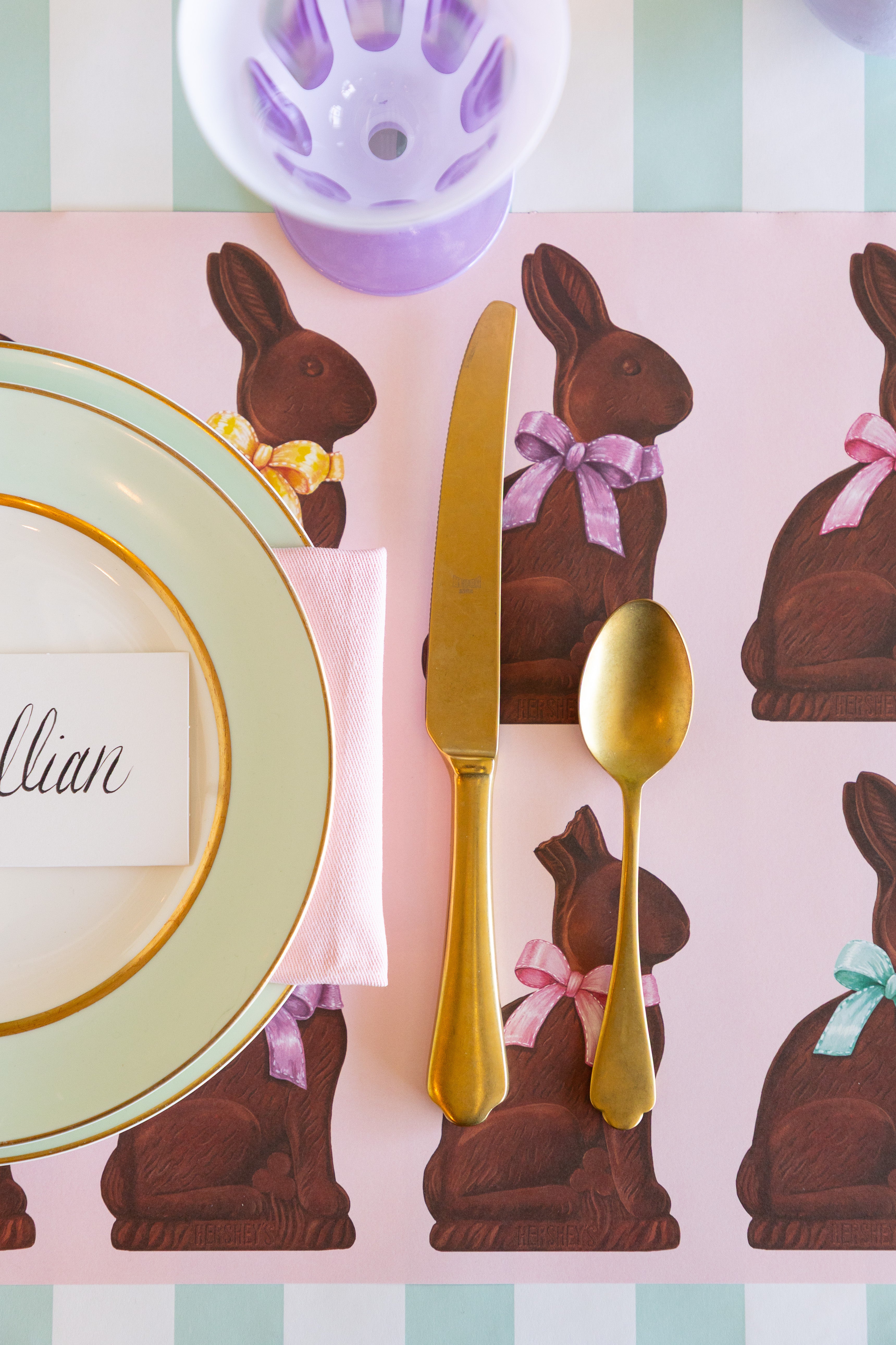 Easter-themed place setting with chocolate bunny placemats, gold cutlery, and pastel colors.