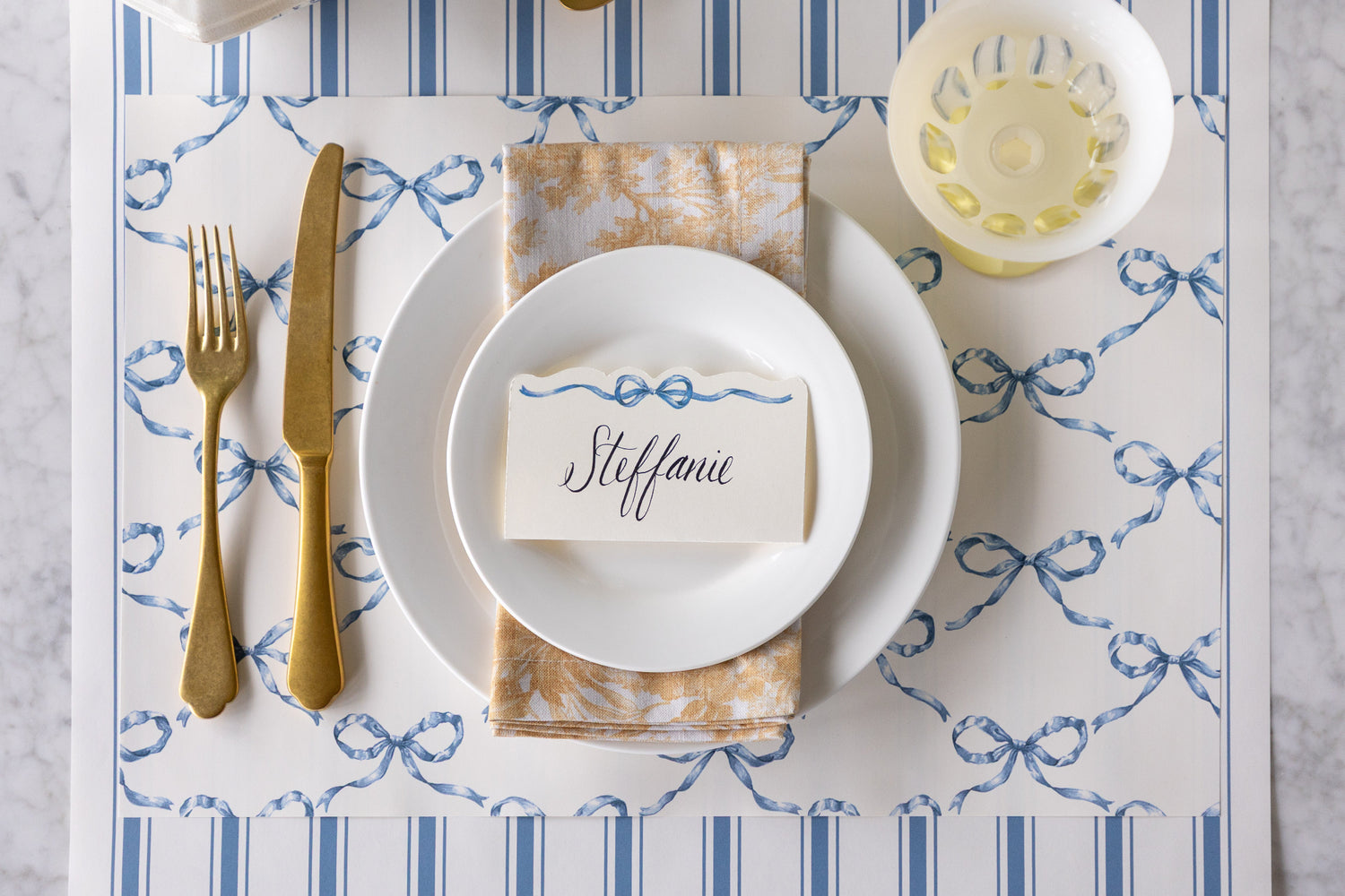 Elegant table setting with Heirloom Blue Bow Lattice Placemat, Heirloom Blue Bow Place Card, Cornflower Blue Linen Stripe Runner and white plates.