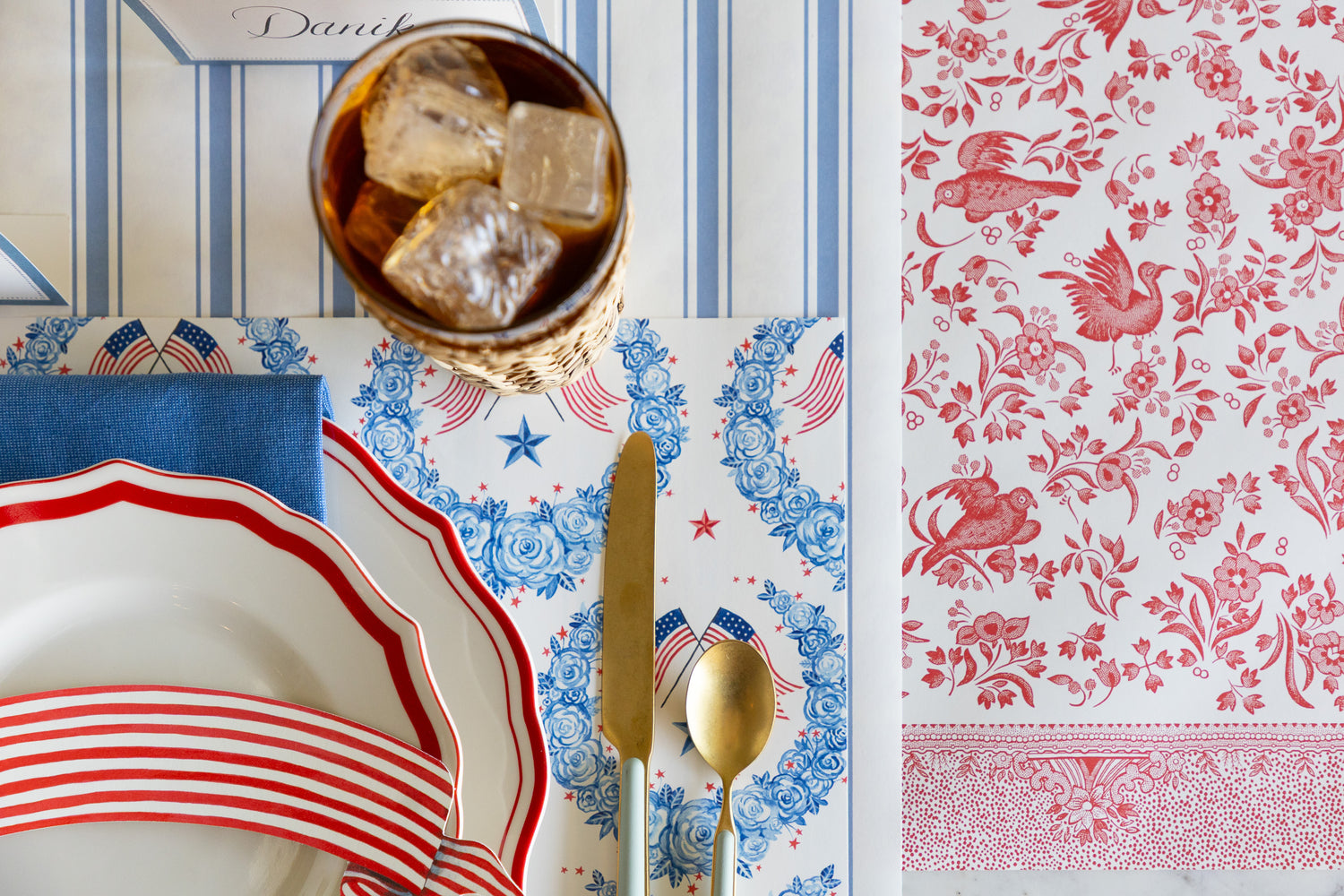 Dinnerware set with red, white, and blue design on a tablecloth with floral and bird pattern.