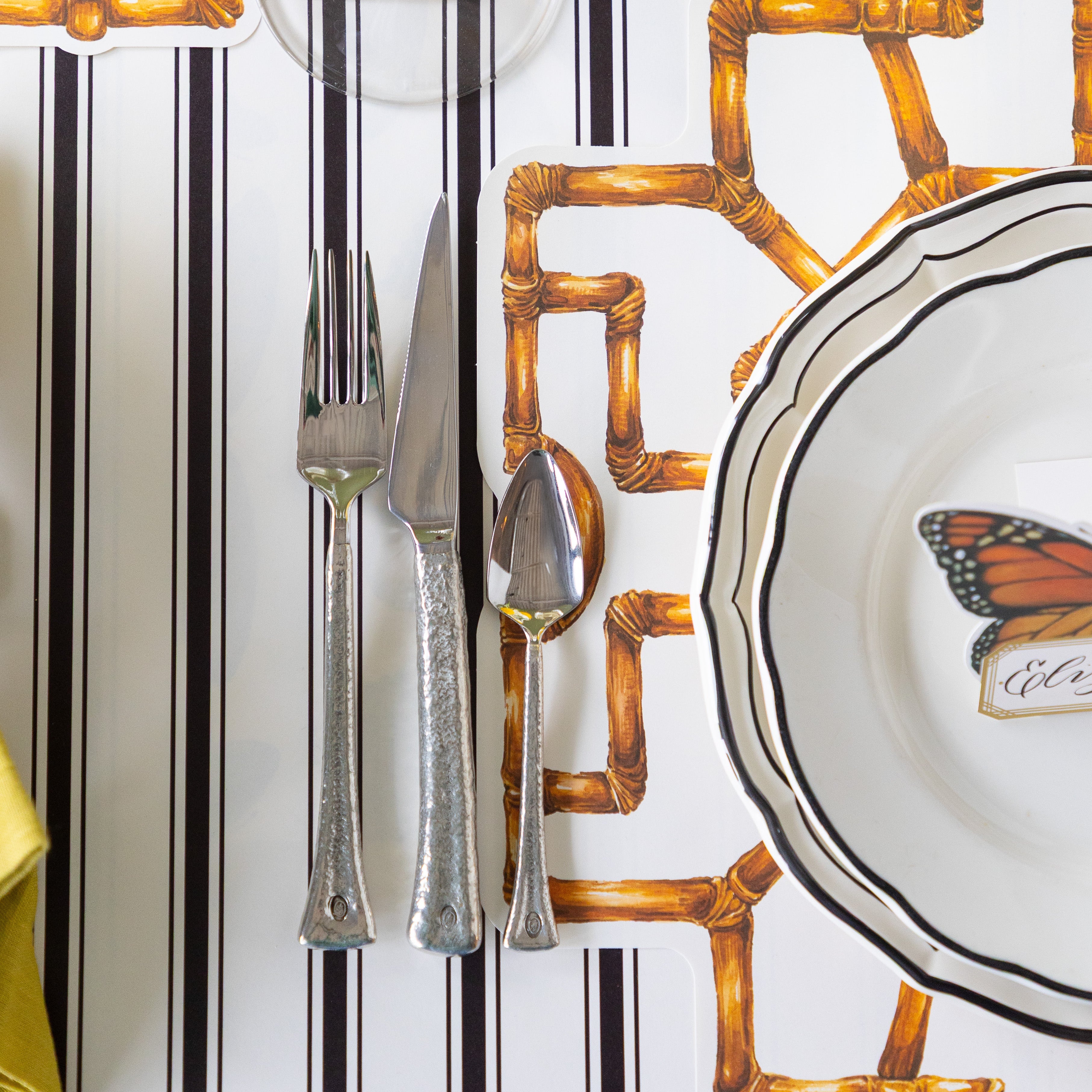 Set table with Die-cut Bamboo Placemat, black rimmed plates and flatware on the Black Linen Stripe Runner.