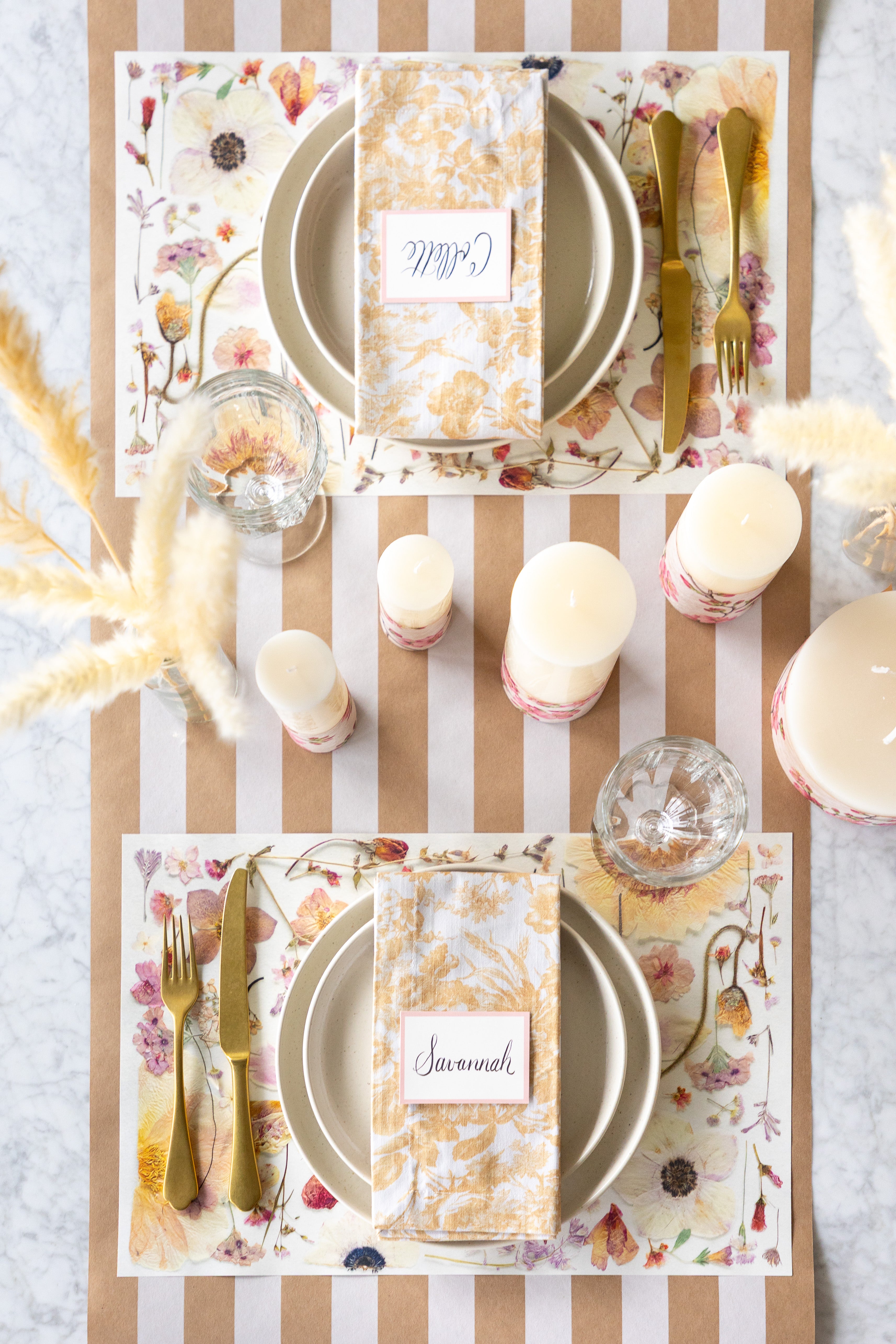 Elegant table setting with Blush Pressed Petals Placemats, gold cutlery, and candles on the Kraft White Classic Stripe Runner.