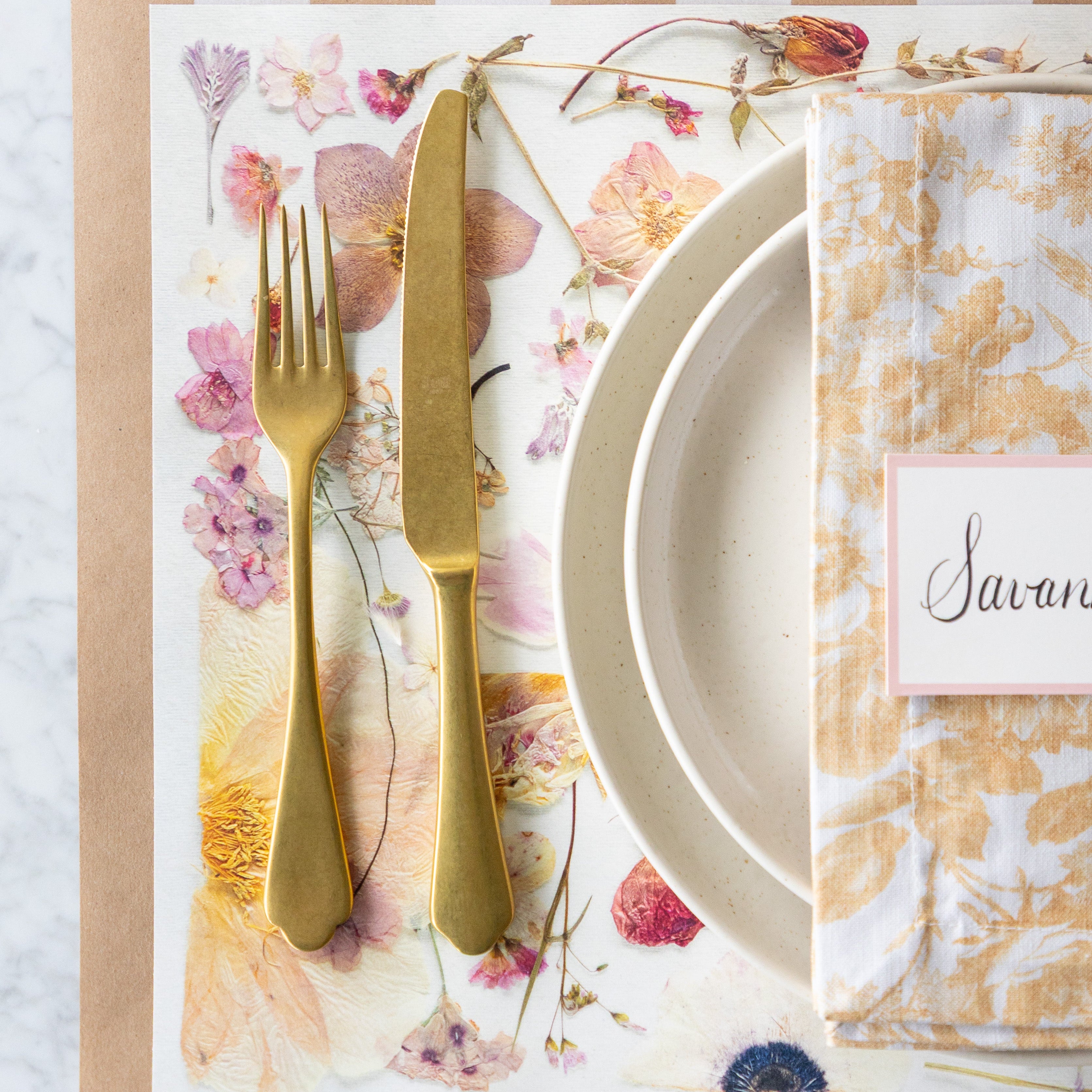 Table setting with floral placemat, gold cutlery, and runner.