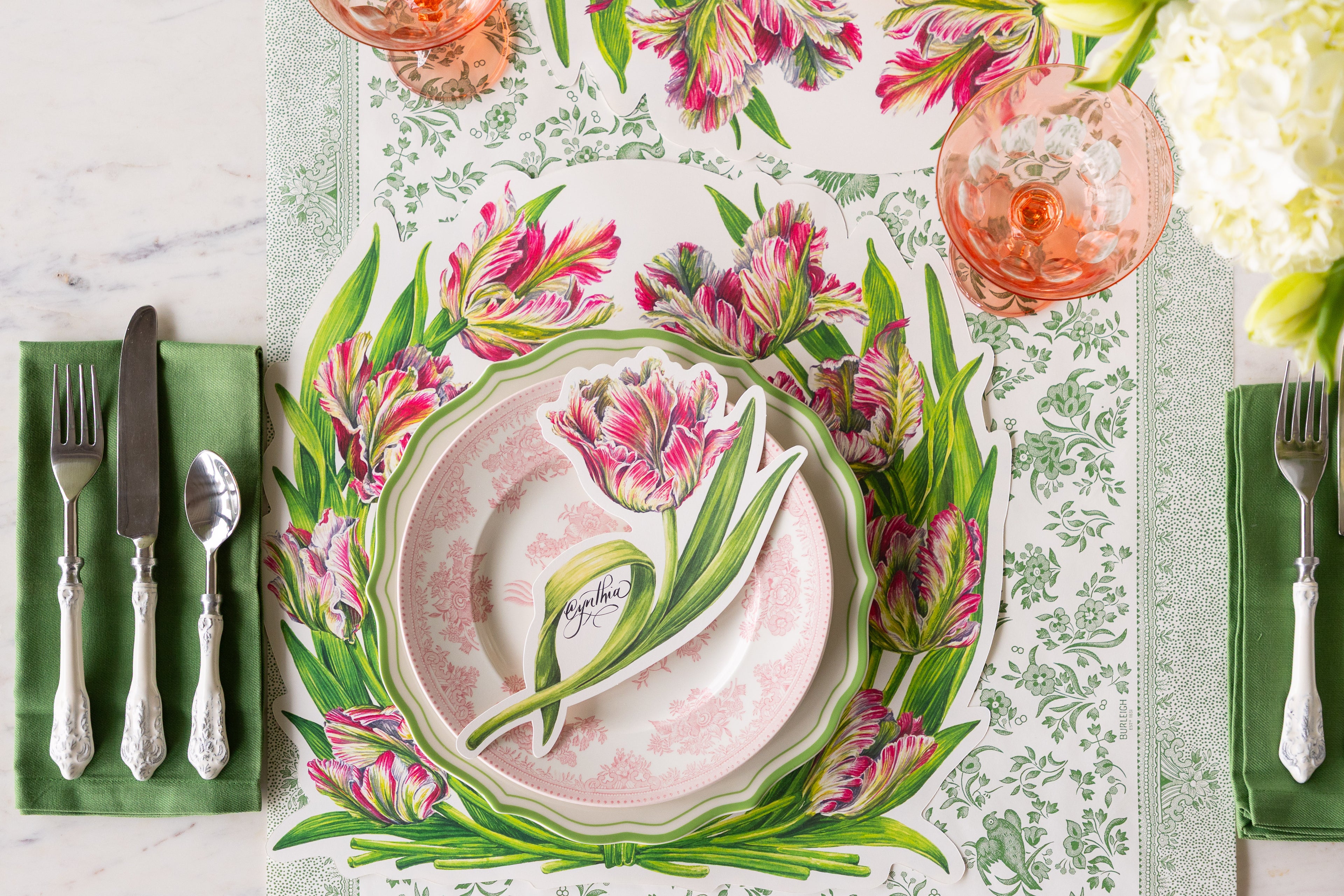 Table set with the Die-cut Parrot Tulip Placemat, green rimmed and pink floral plate, Parrot Tulip Table Accent, flowers, a green napkin and vintage flatware on the Green Regal Peacock Runner.