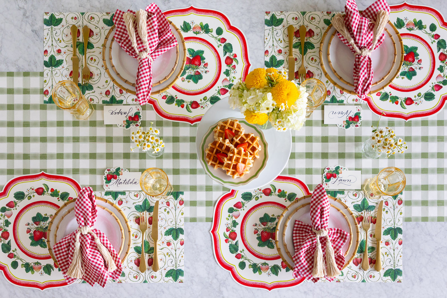 Decorative table setting with waffles, flowers, Die-cut Strawberry China and Strawberry Fields Placemats, Strawberries Place Cards, red checkered napkins and gold cutlery on the Moss Painted Check Runner.