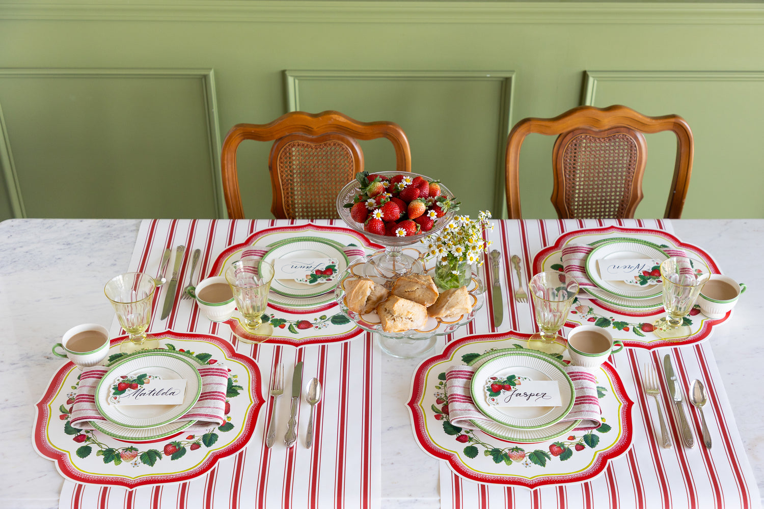 Dining table set with strawberries, scones and flowers, Die-cut Strawberry China Placemats, green rimmed dinnerware, red striped napkin and vintage silverware on the Red Linen Stripe Runner.