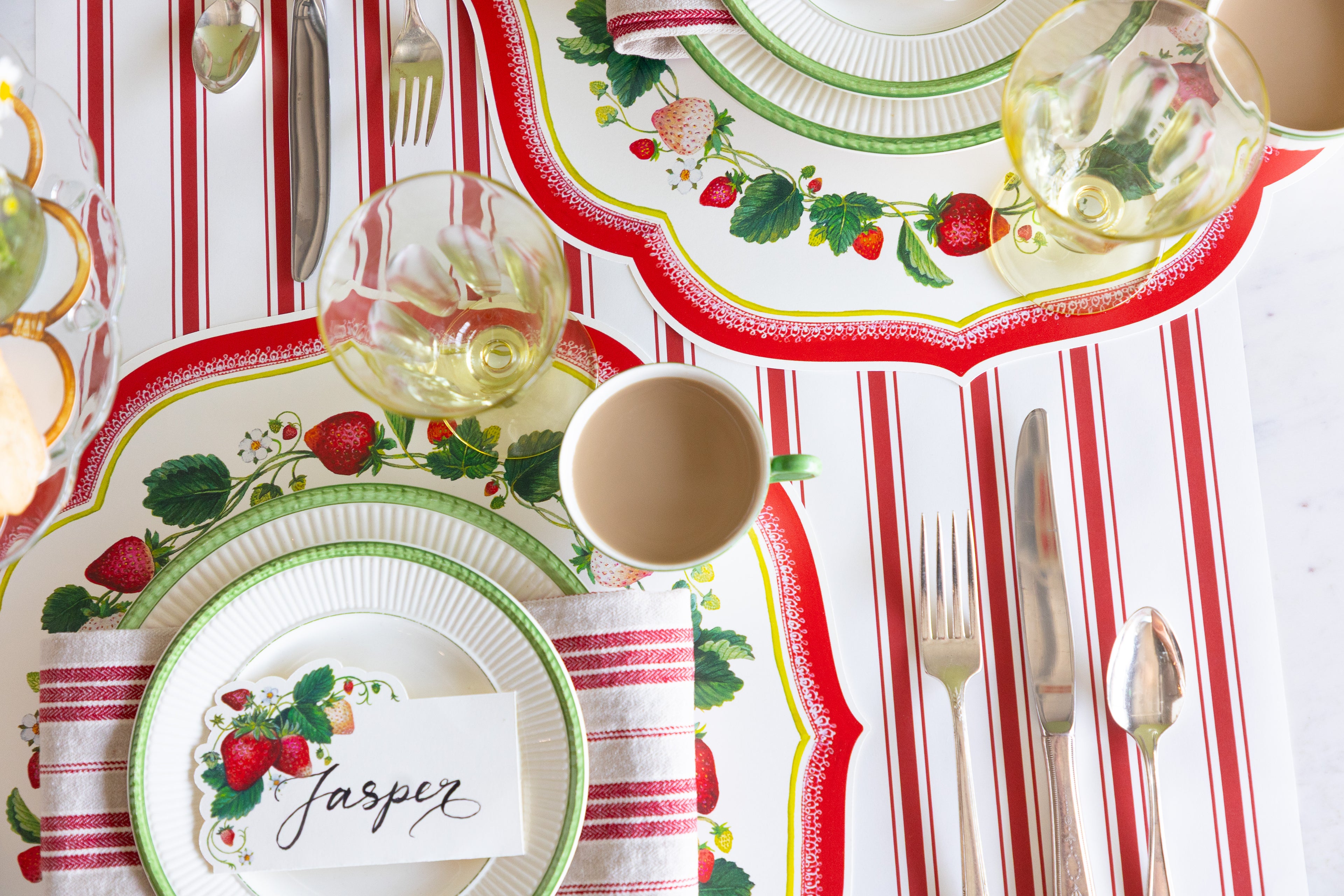 Place setting with Die-cut Strawberry China Placemats, green rimmed dinnerware, red striped napkin and vintage silverware on the Red Linen Stripe Runner.
