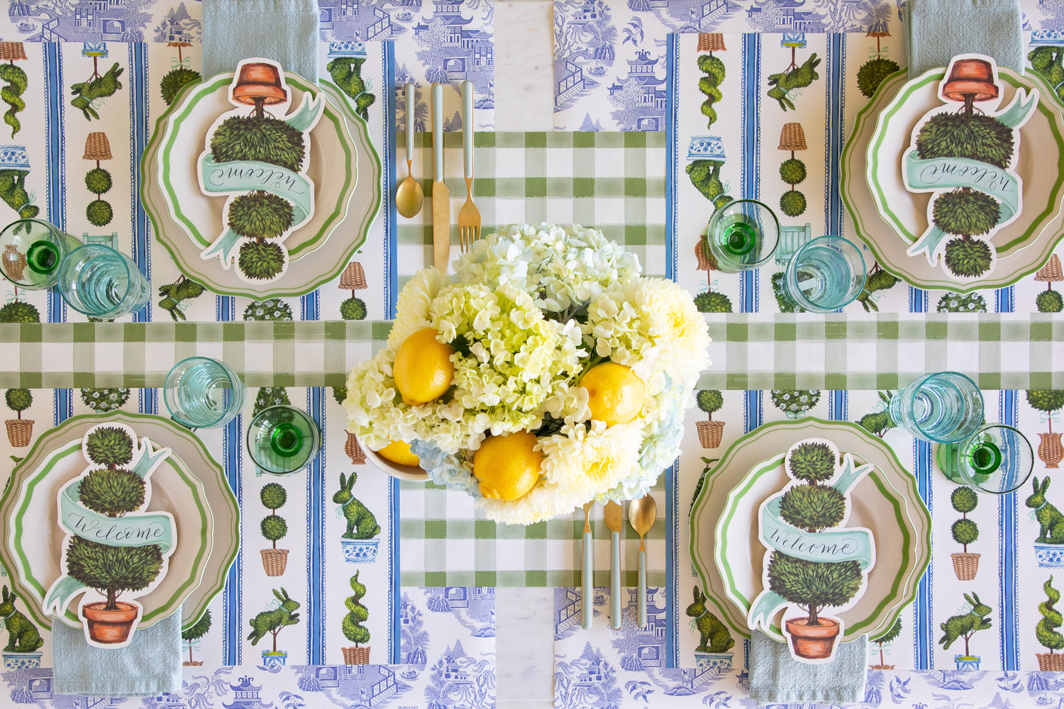 Table setting with a floral centerpiece, Spring Topiary Placemats, Topiary Table Accents, Green Icing on the Cake Plates, seafoam napkins and cutlery on the Moss Painted Check and Blue Regal Peacock Runners.
