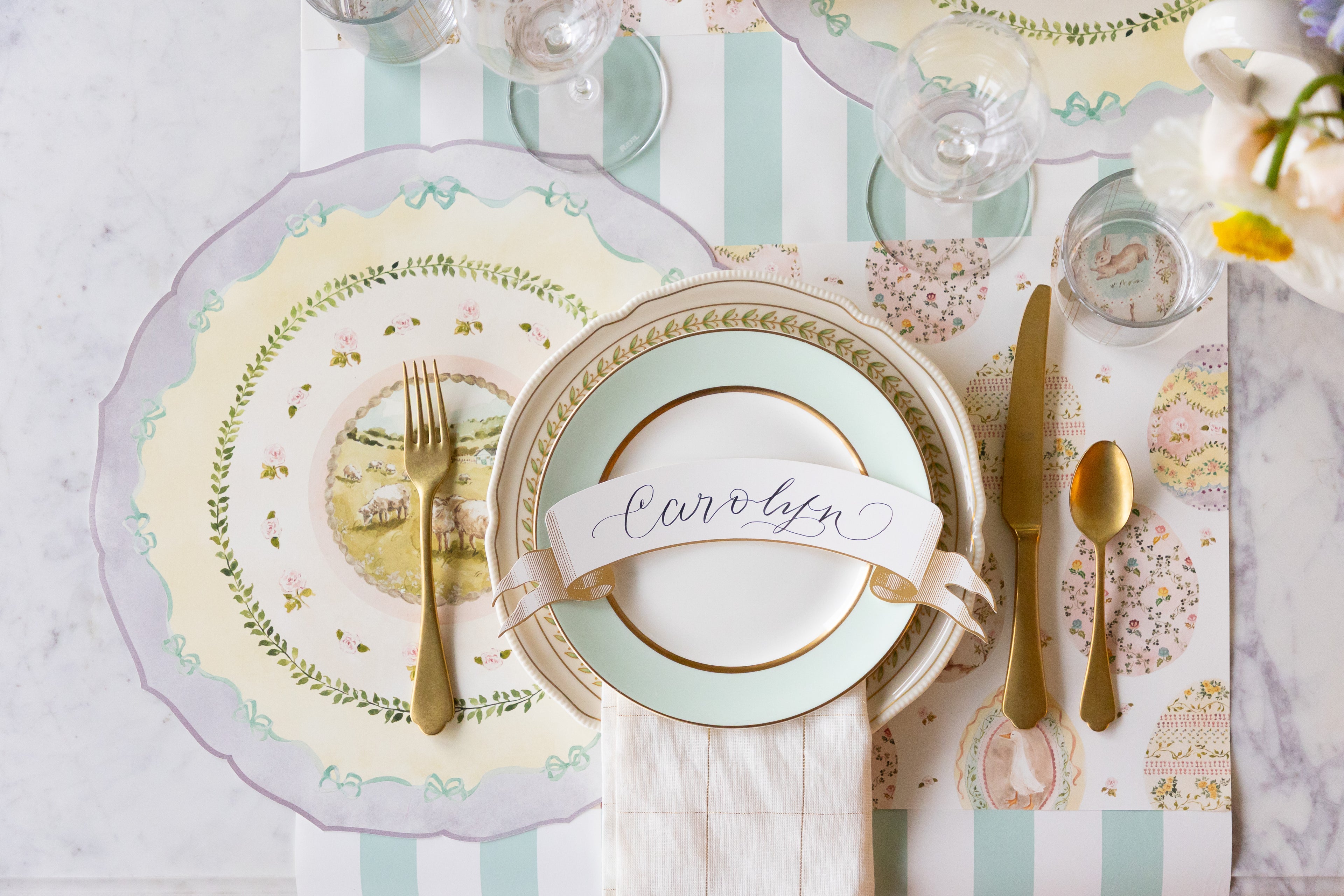Elegant table setting with gold cutlery, decorative plates, Die-cut Spring Meadow and Sweet Spring Eggs Placemats and Classic Gold Banner Table Accent on the Seafoam Classic Stripe Runner.