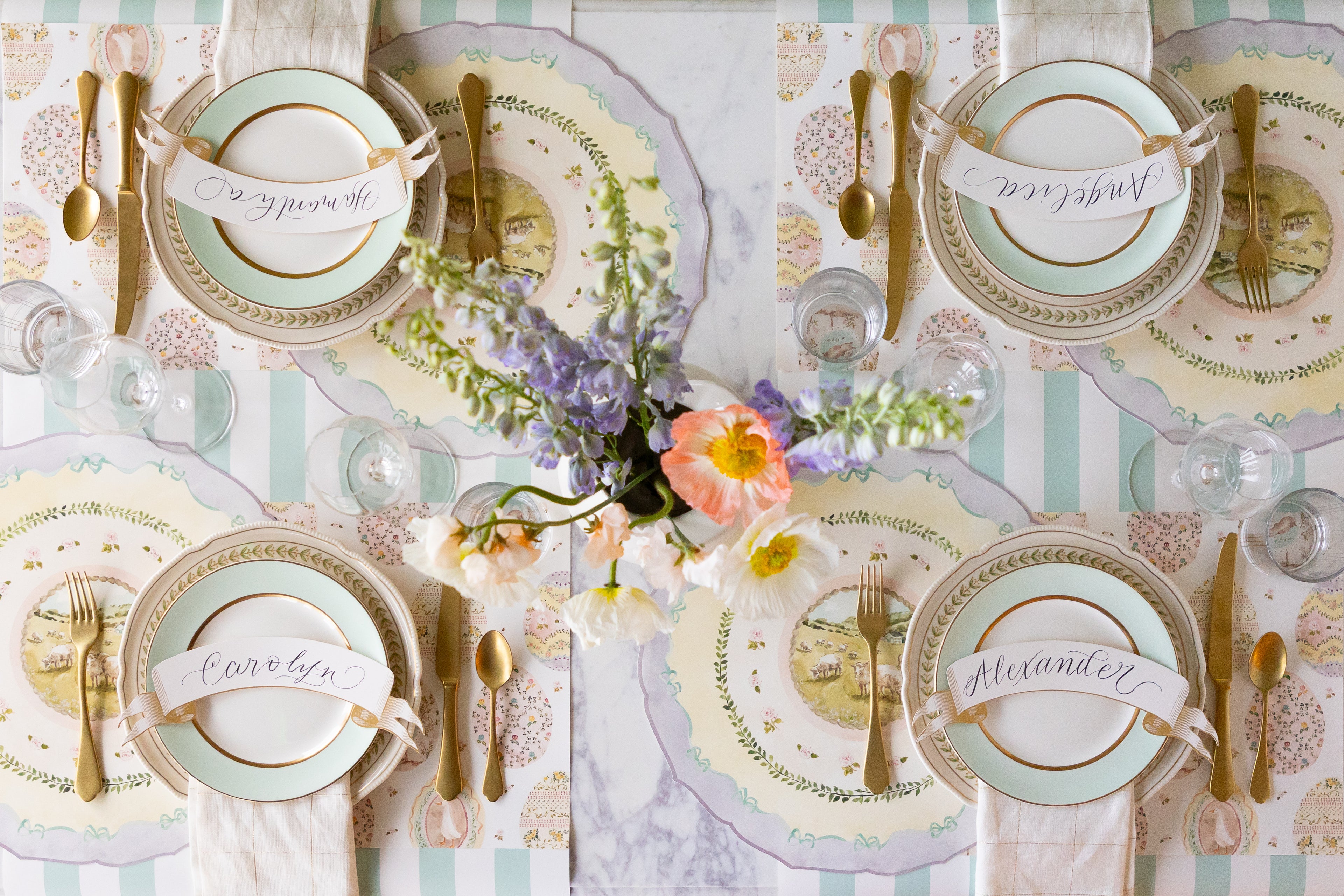 Decorative table setting with Die-cut Spring Meadow Placemats, Classic Gold Banner Table Accents, decorative plates, flowers, and cutlery on the Seafoam Classic Stripe Runner.