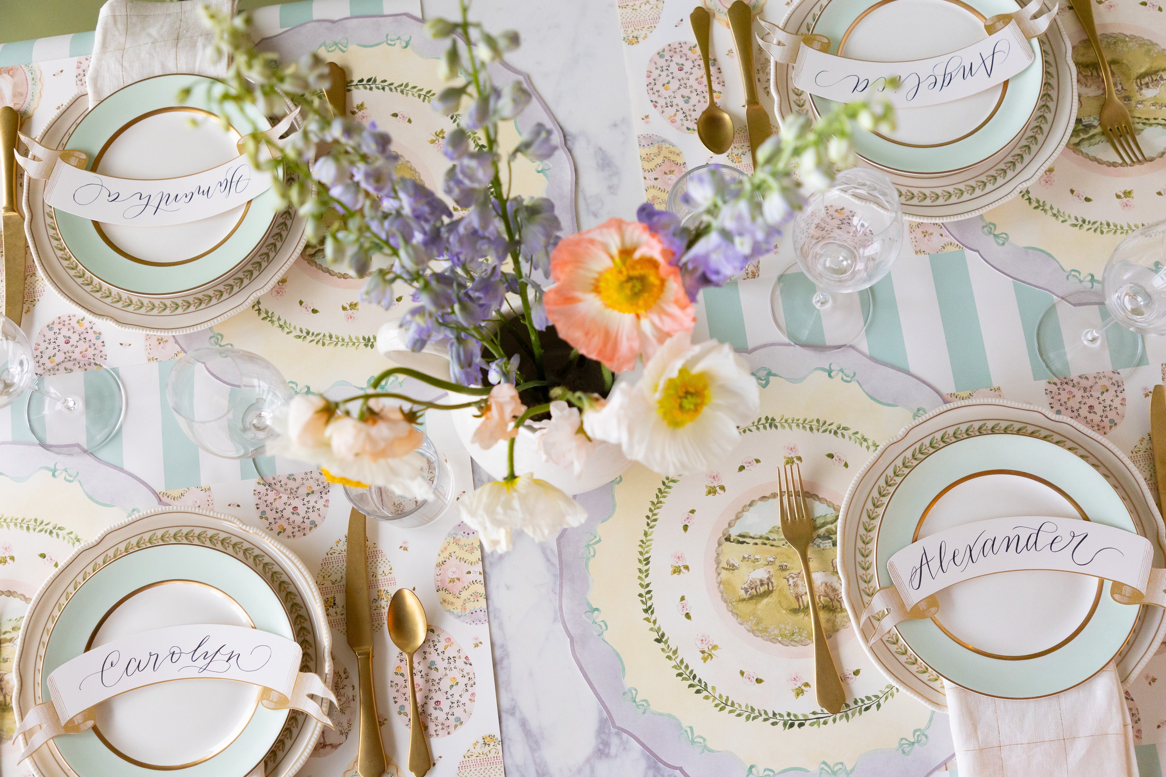 Decorative table setting with Die-cut Spring Meadow Placemats, Classic Gold Banner Table Accents, decorative plates, flowers, and cutlery on the Seafoam Classic Stripe Runner.