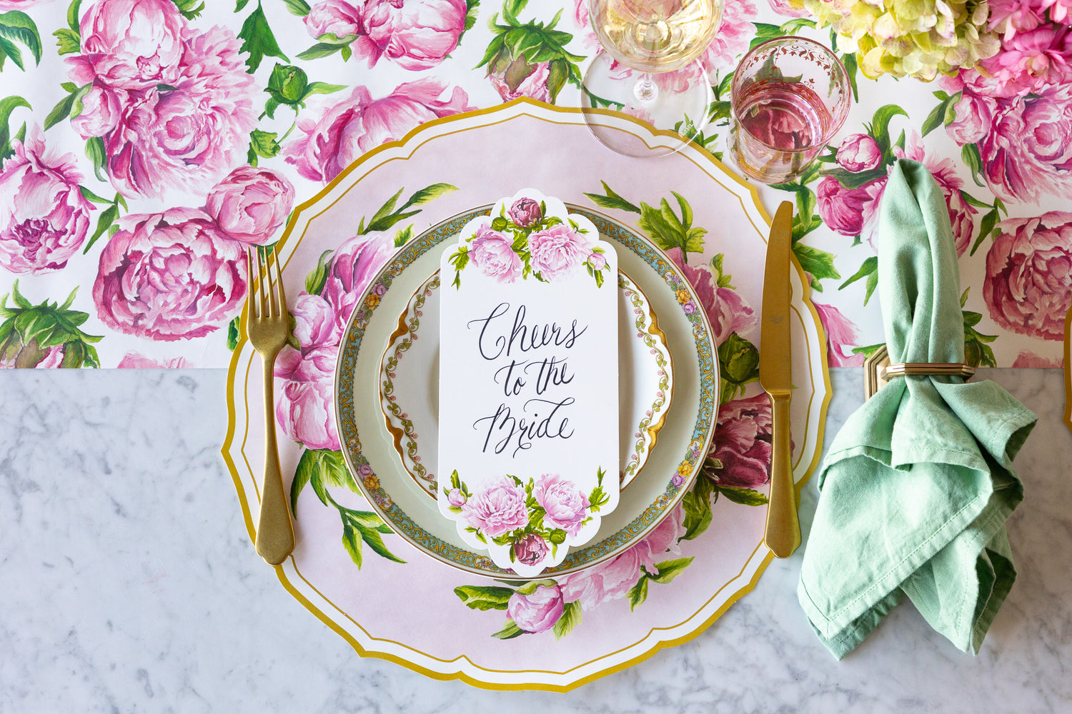Decorative table setting with the Die-cut Peony China Placemat, floral plates, gold flatware and Peonies Table Card with "Cheers to the Bride" on the Peonies in Bloom Runner.
