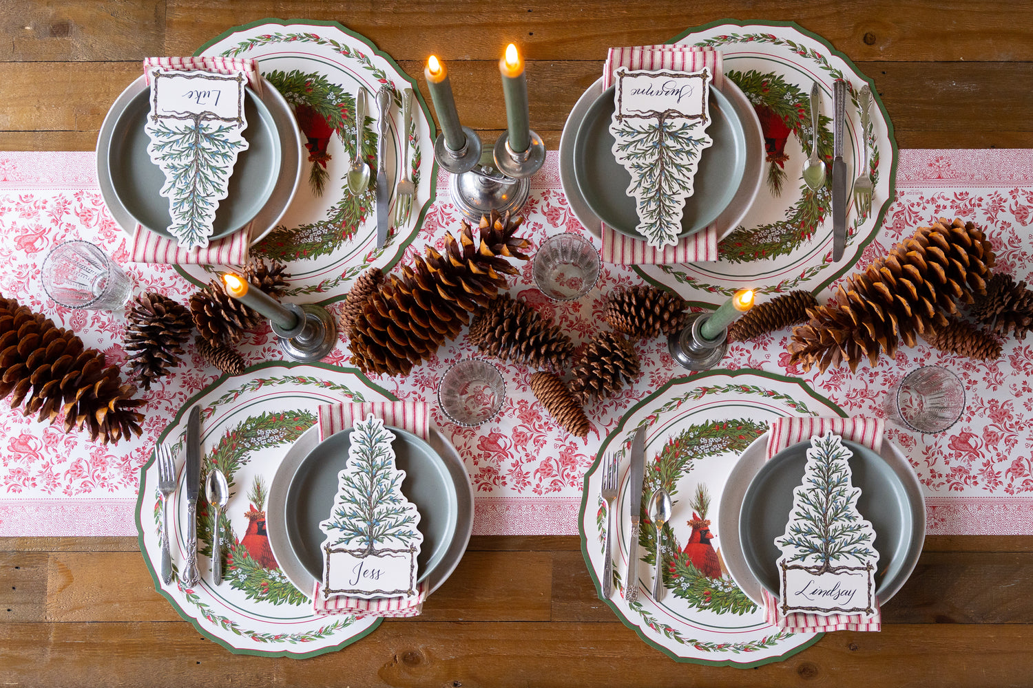 Christmas-themed table setting with place cards and pine cones on a striped table runner. 
