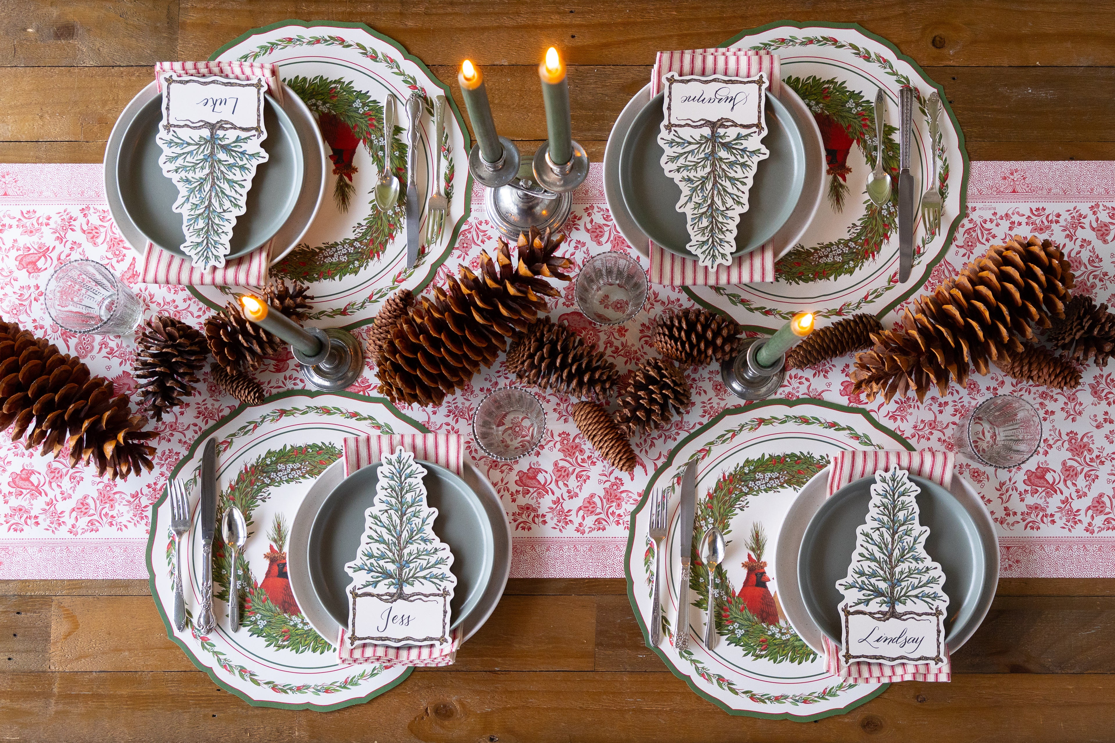 Christmas-themed table setting with place cards and pine cones on a striped table runner. 