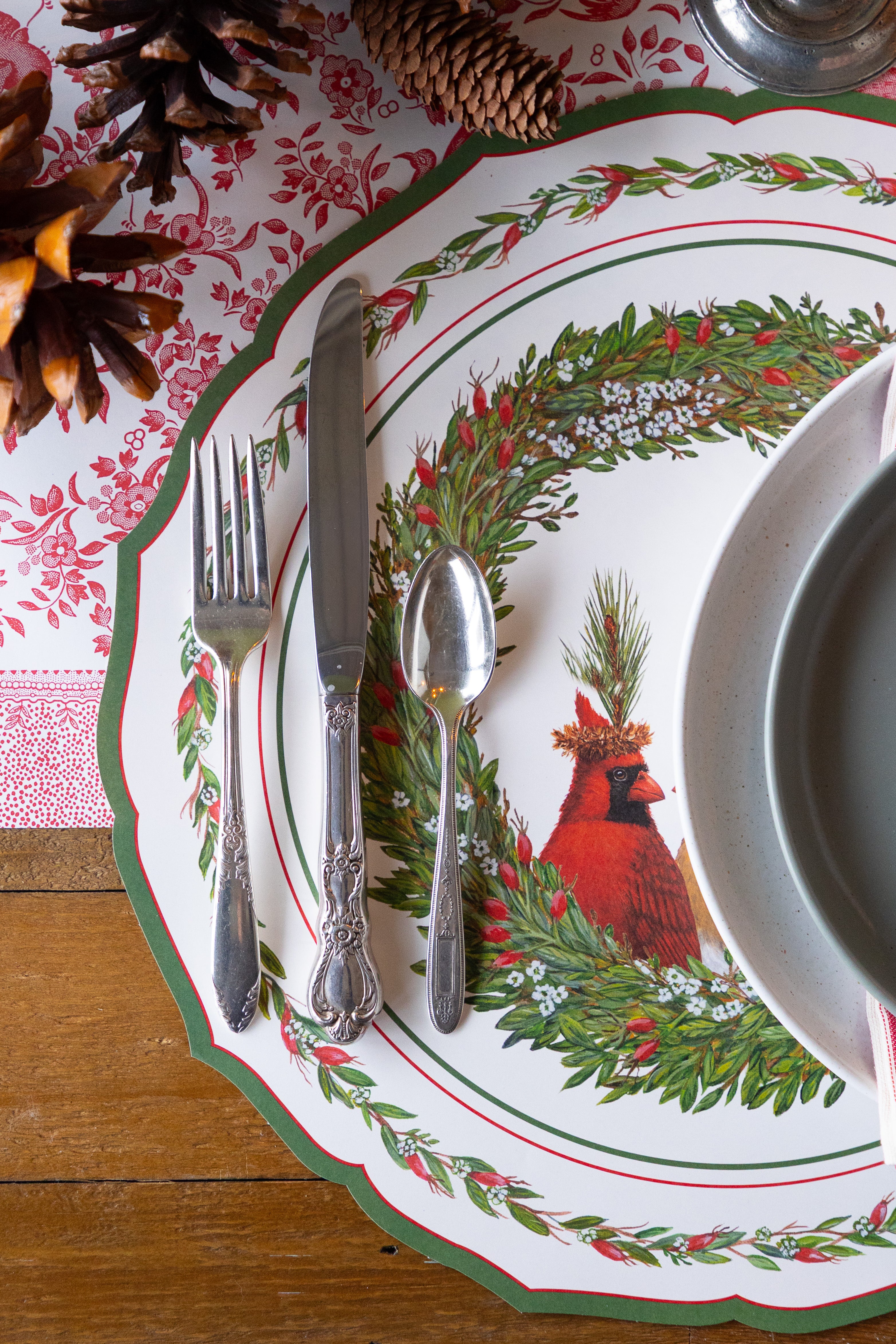 Christmas-themed place setting with silver china on a red patterned runner. 