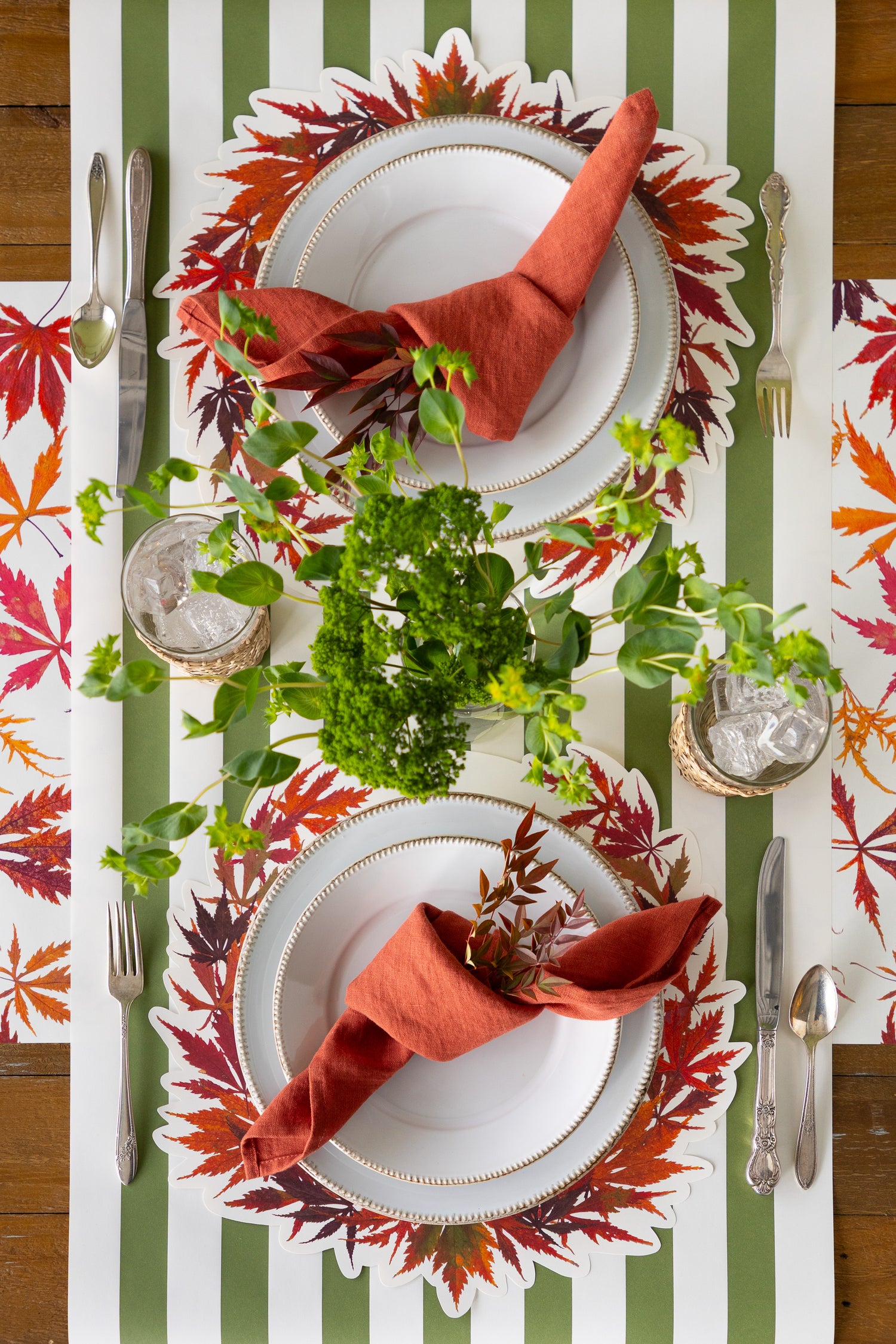 Table setting with 2 place settings and the Die-cut Japanese Maple Wreath Placemats and greenery in the middle. 
