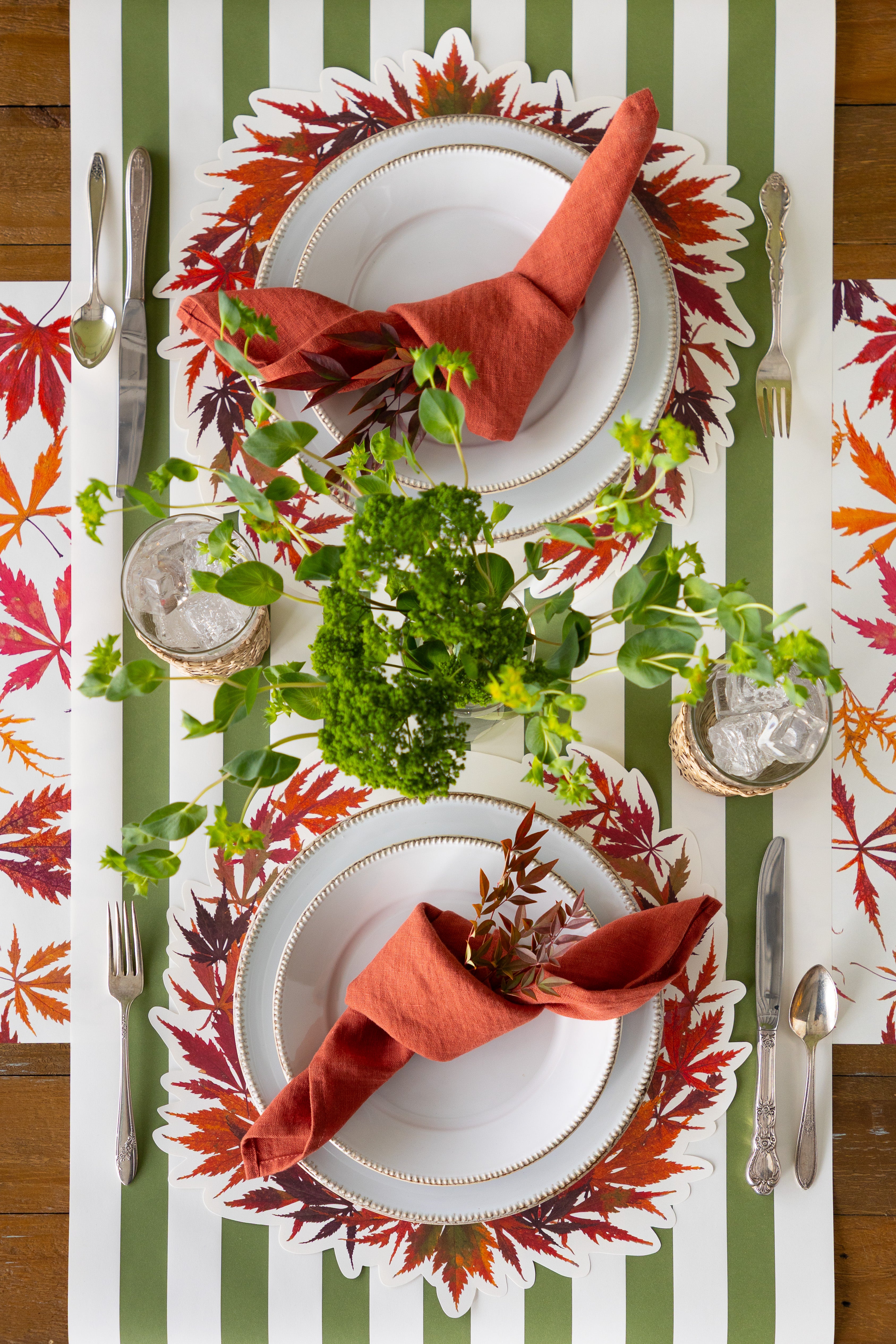 Table setting with 2 place settings and the Die-cut Japanese Maple Wreath Placemats and greenery in the middle. 