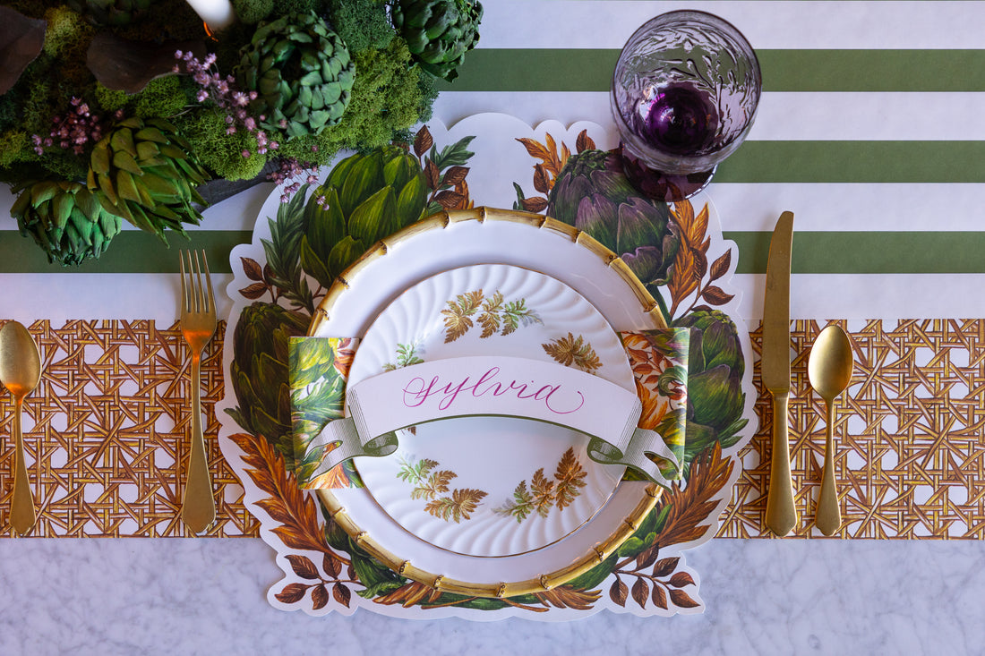 Decorative table setting with a place card, cutlery, and floral arrangement on a striped tablecloth.