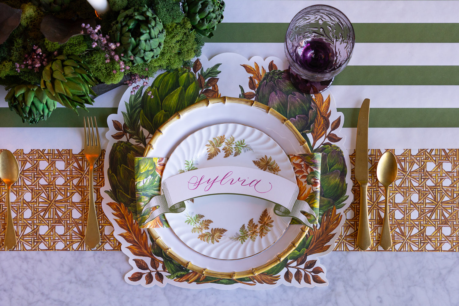 Decorative table setting with a place card, cutlery, and floral arrangement on a striped tablecloth.