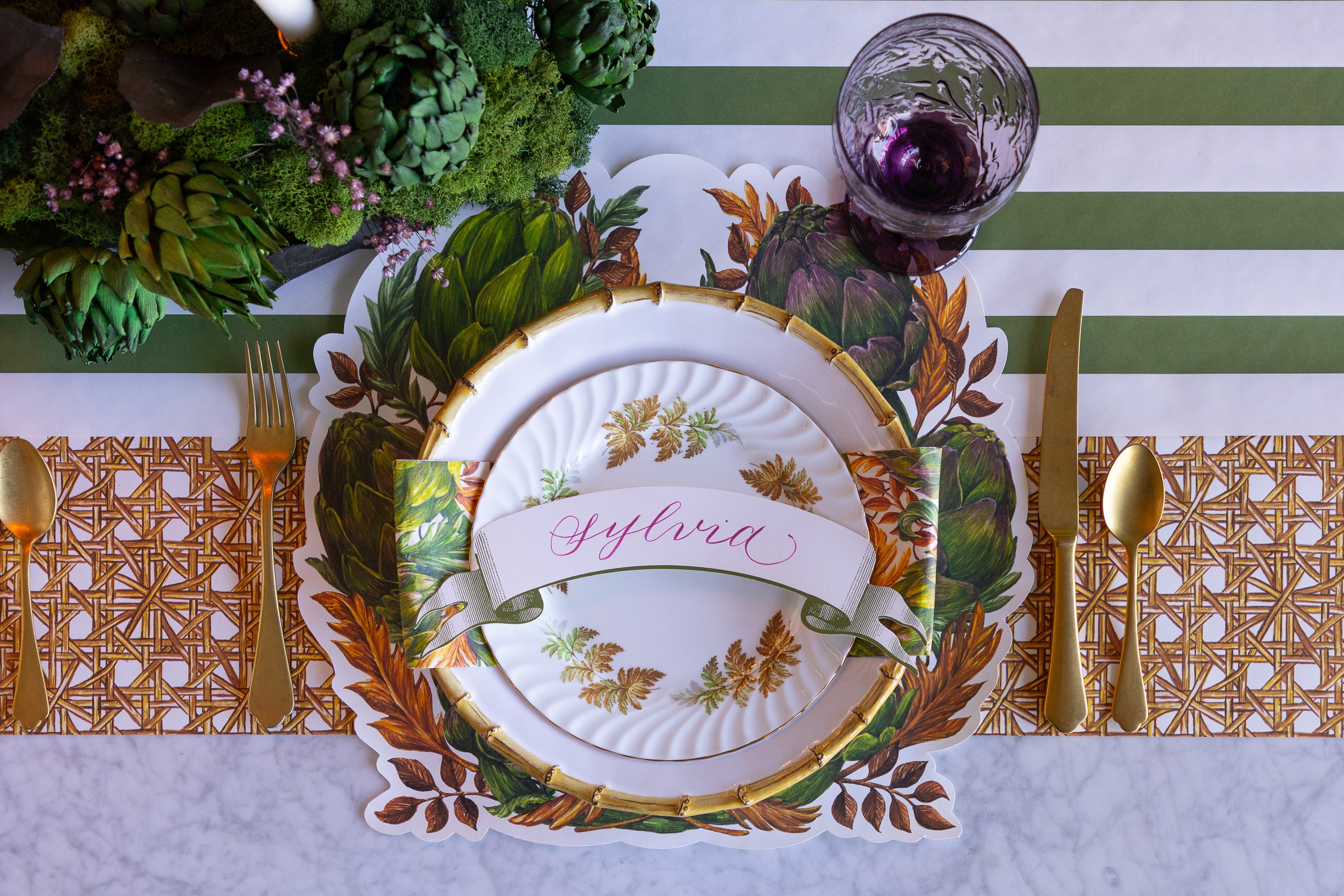 Decorative table setting with a place card, cutlery, and floral arrangement on a striped tablecloth.
