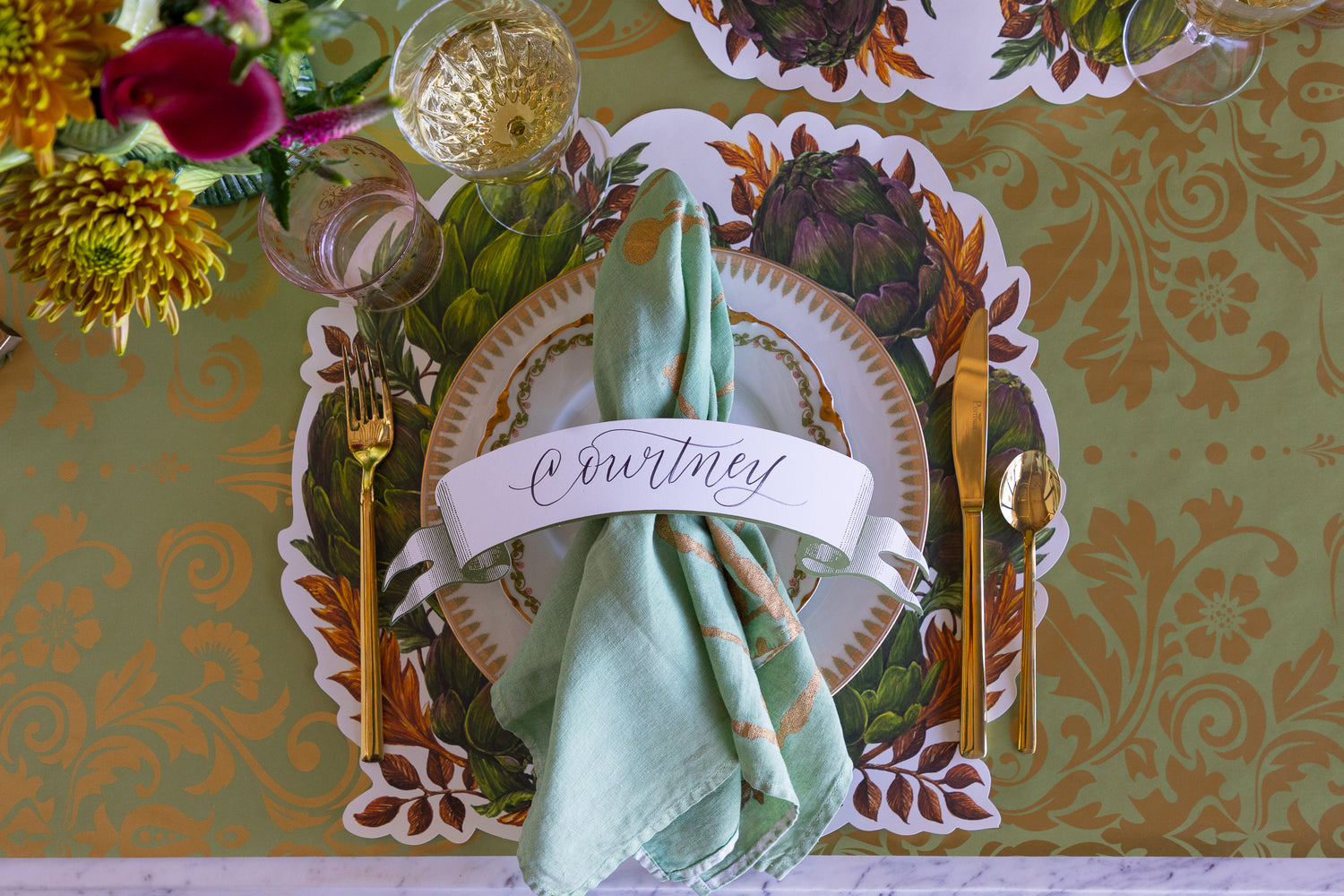 Decorative table setting with a name card, green napkin, and floral patterned placemat.