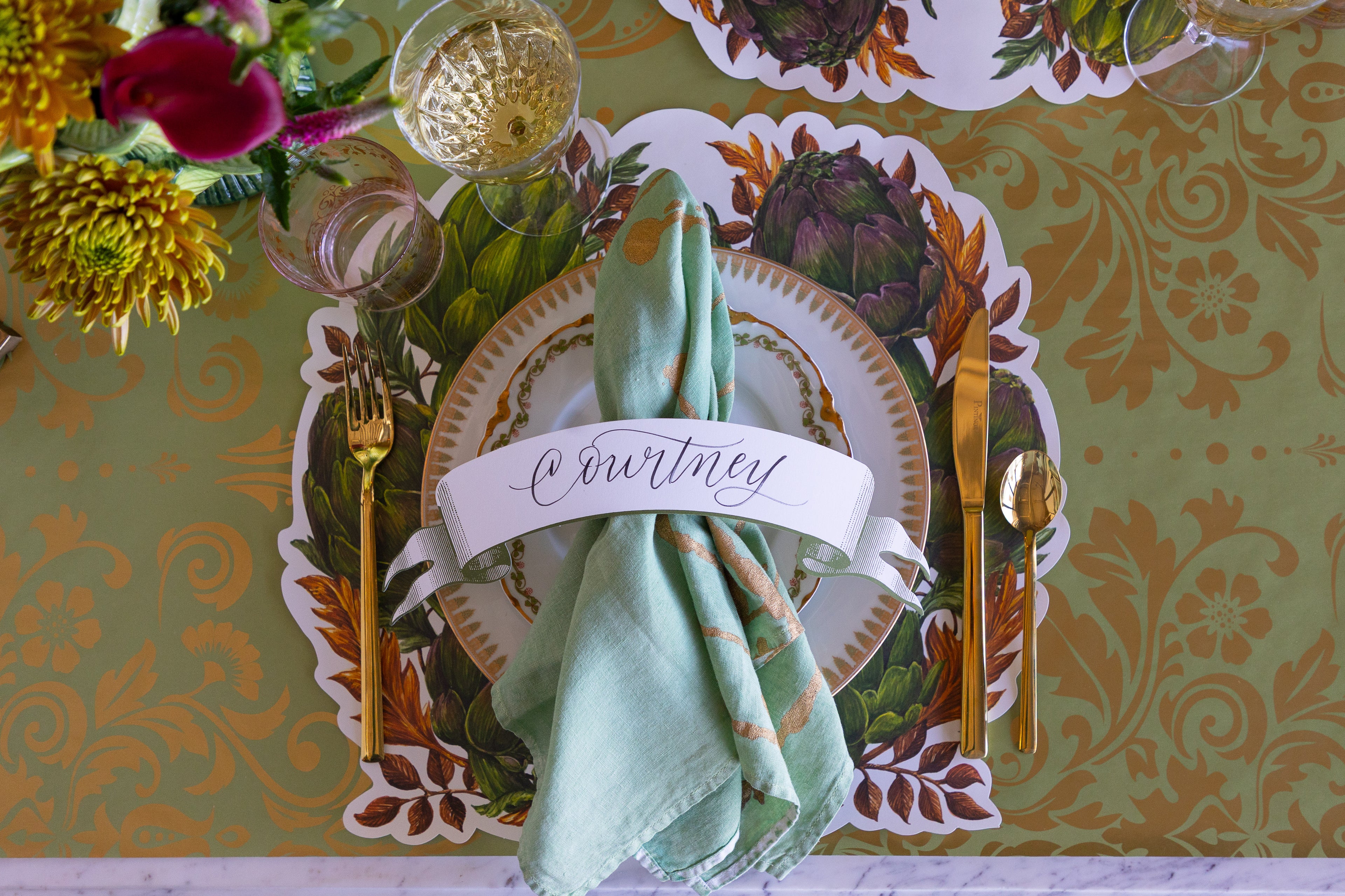 Decorative table setting with a name card, green napkin, and floral patterned placemat.