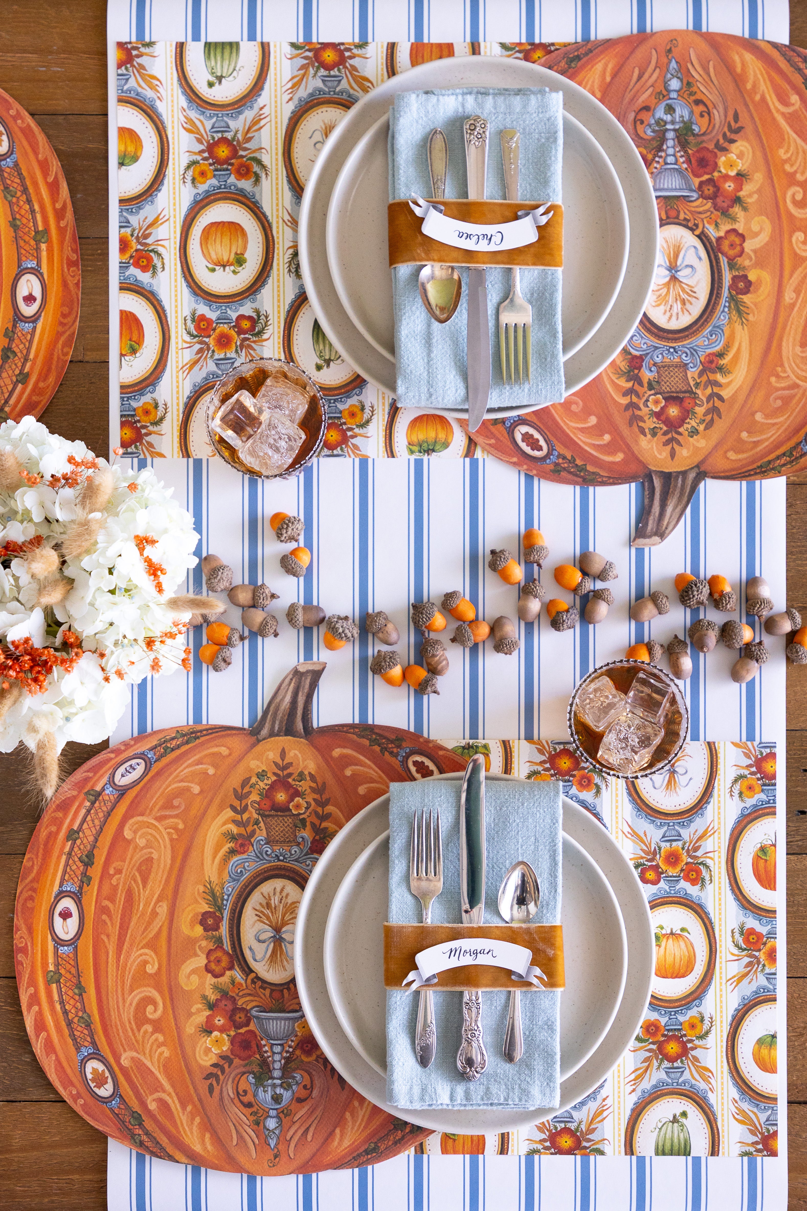 Thanksgiving table setting with pumpkin placemats,  acorns and cutlery on a striped table runner.