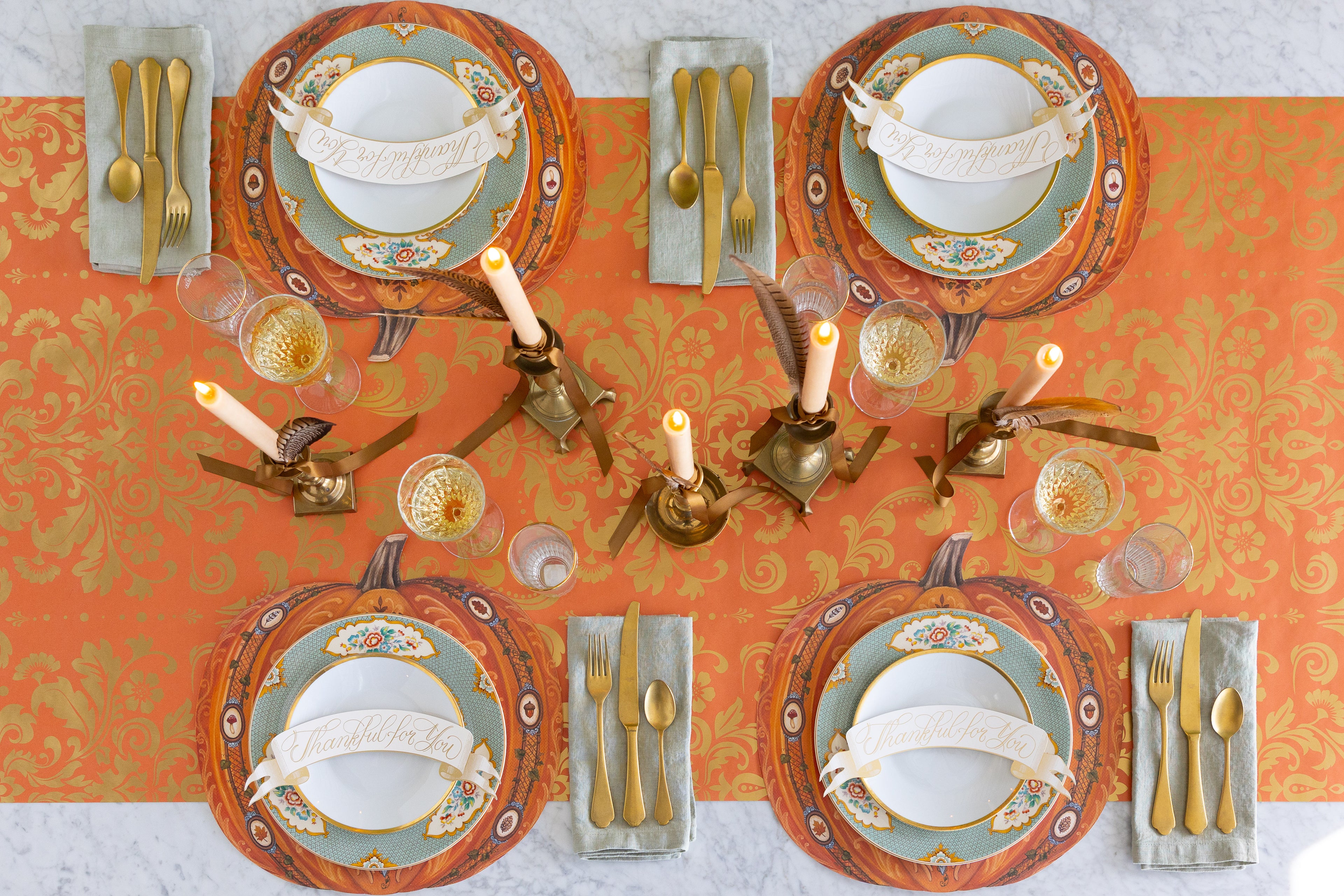 Decorative table setting with plates, cutlery, and candles on an orange and gold patterned table runner.