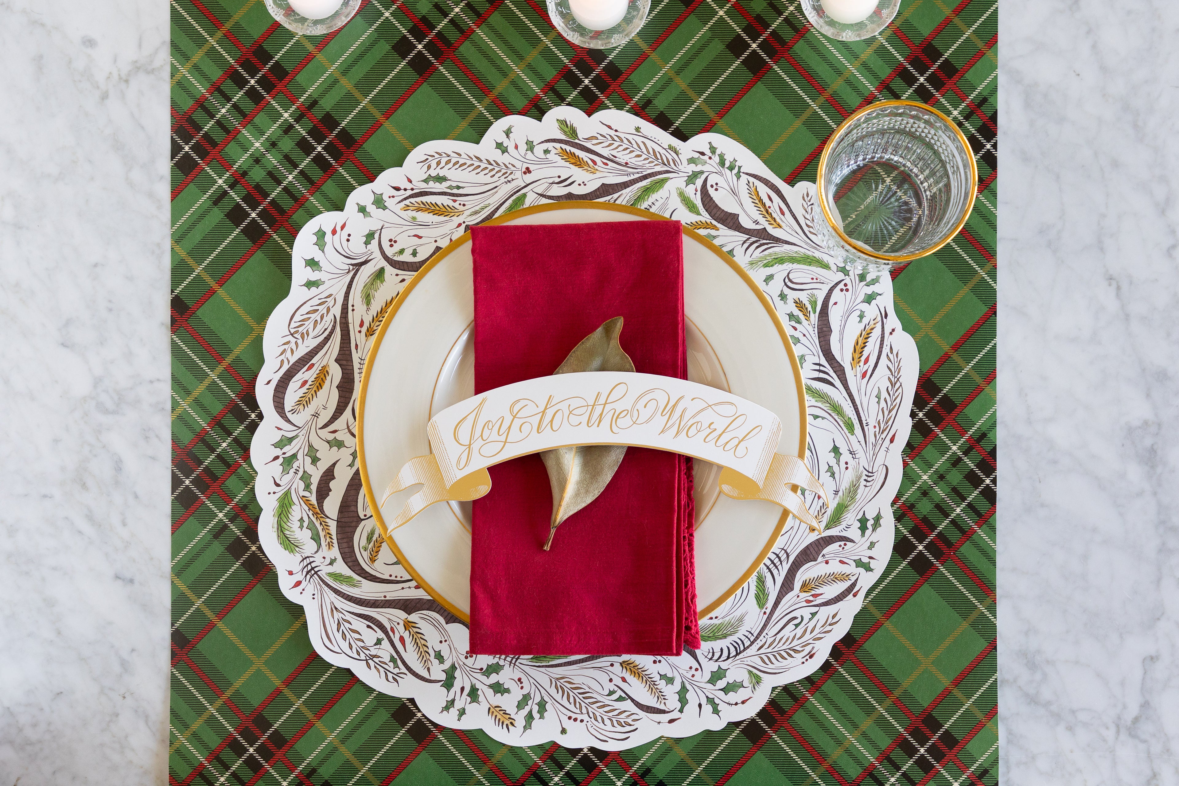 Decorative place setting with a red napkin, gold ribbon, and plaid table runner.